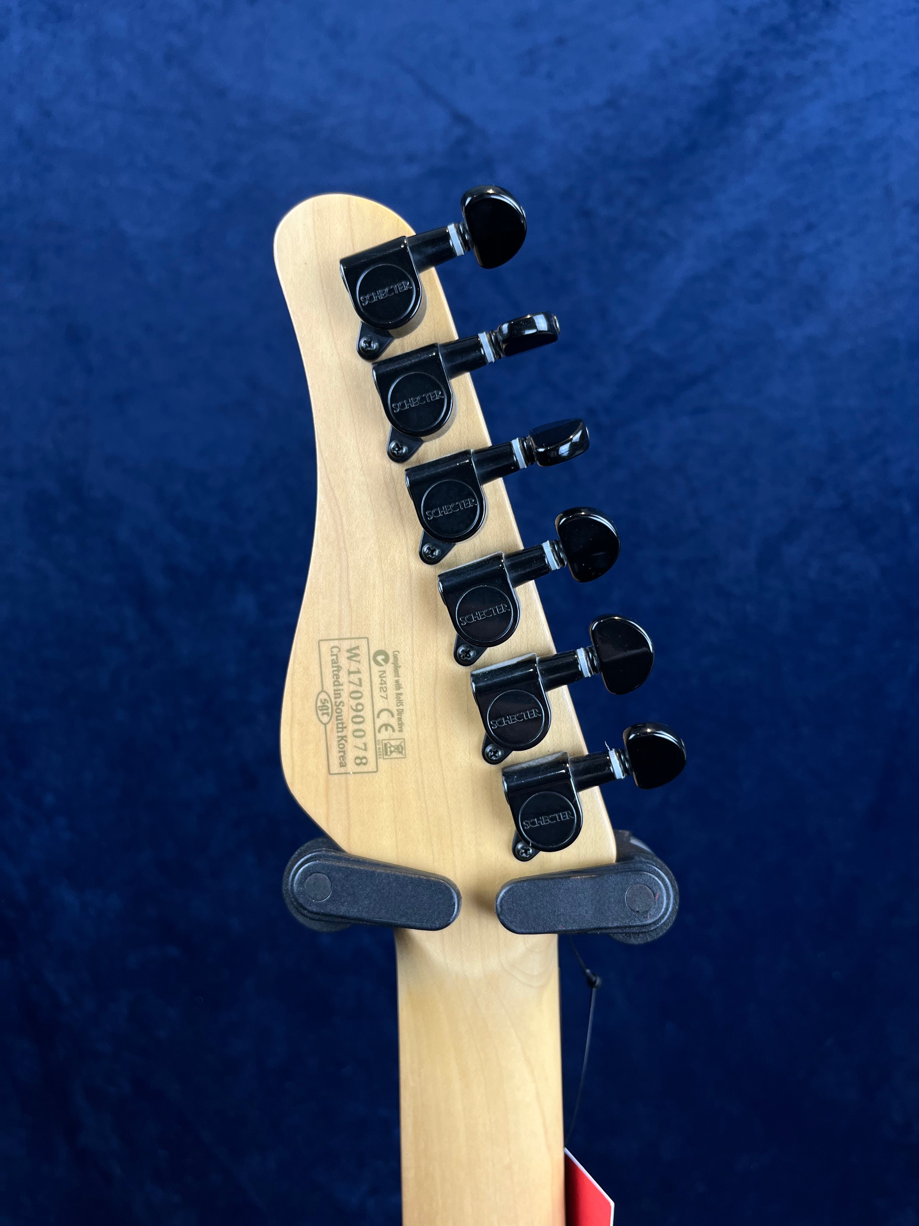 Five black tuning pegs on the back of a Schecter electric guitar headstock, light wood finish, serial number and logo markings visible.