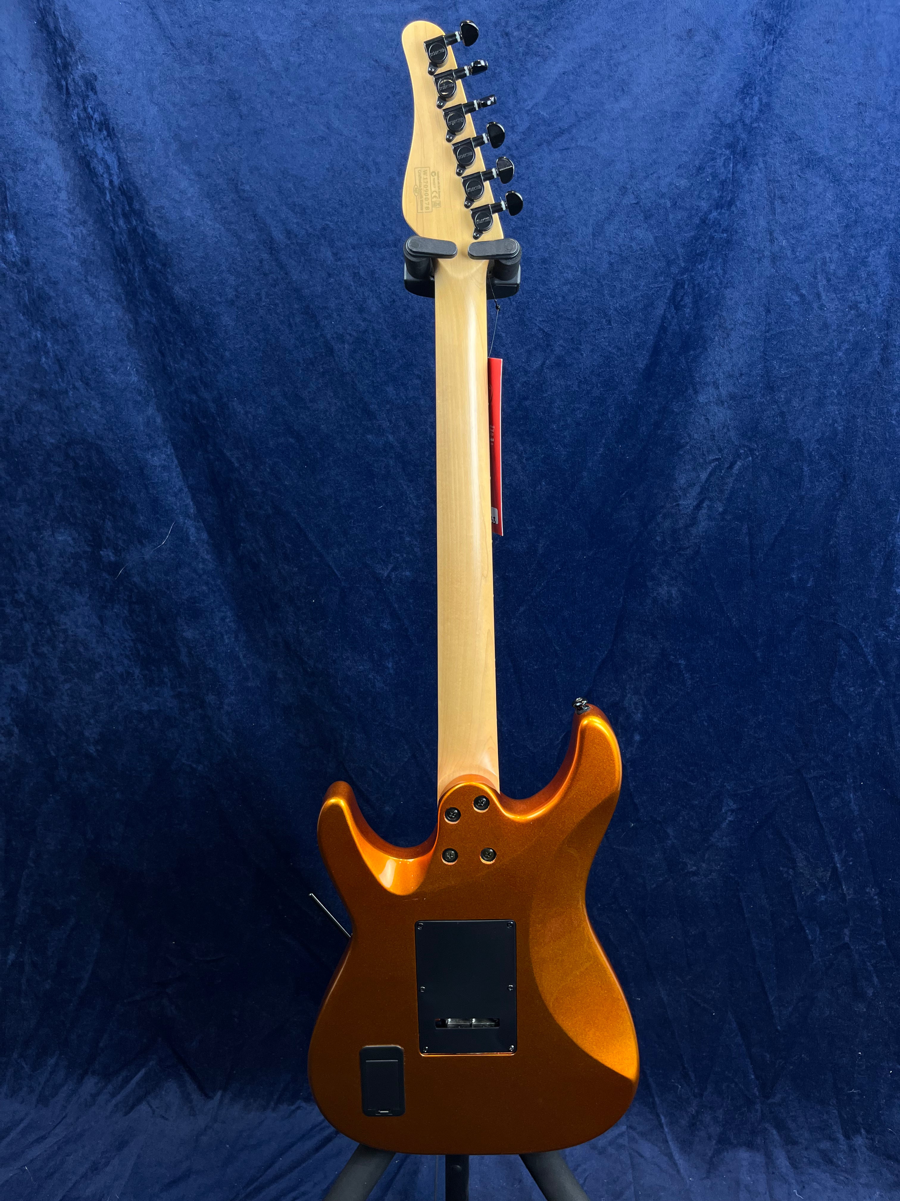 Glossy metallic orange electric guitar shown from the back, with a natural maple neck, six black tuning pegs, and a blue textured background.