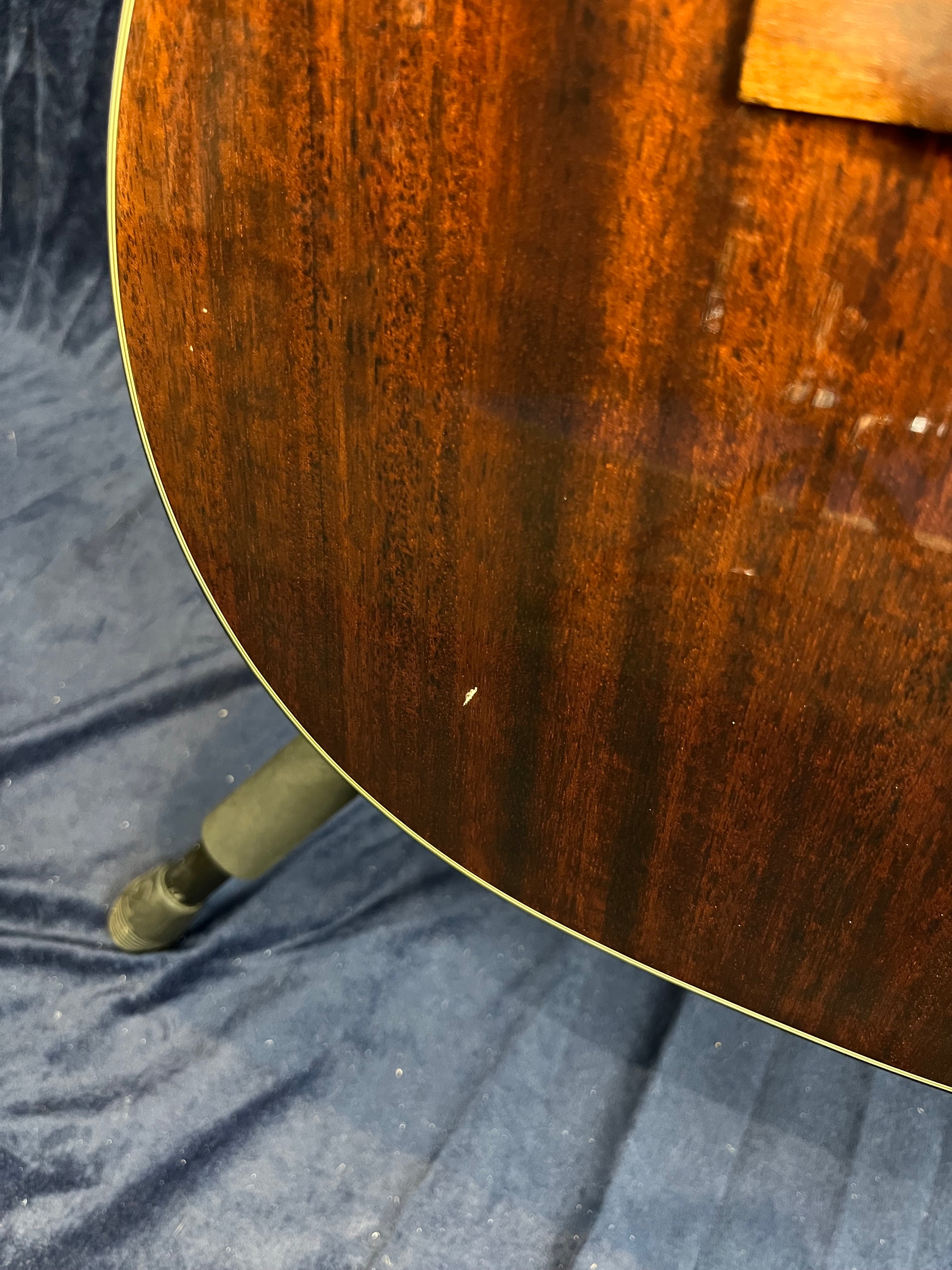 Close-up of a dark wood acoustic guitar body with a small white ding on the surface, shown against a dark fabric background.