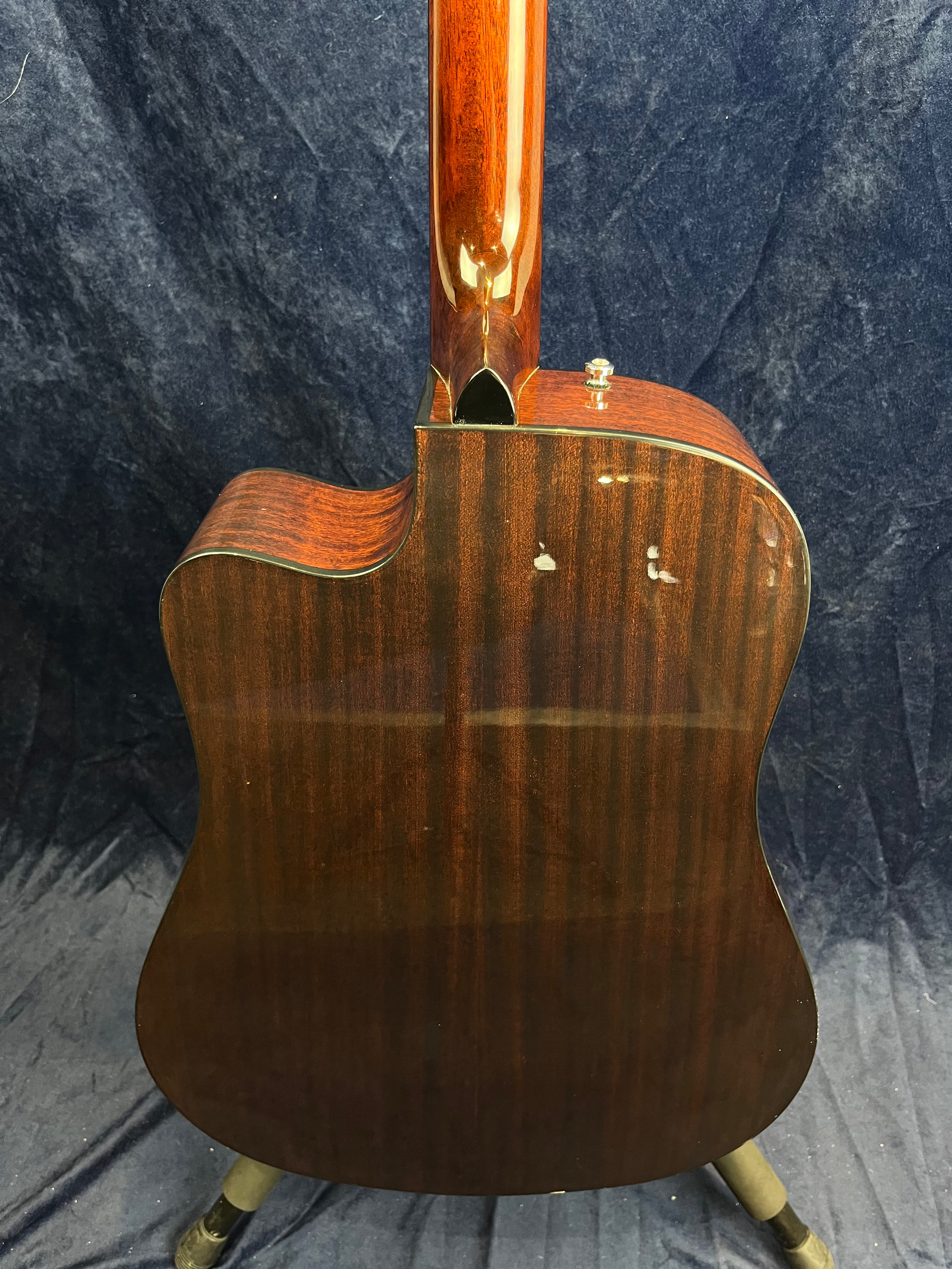 Polished dark wood acoustic guitar back with visible wood grain, a cutaway on the upper left, and minor dings in the finish near the neck joint.
