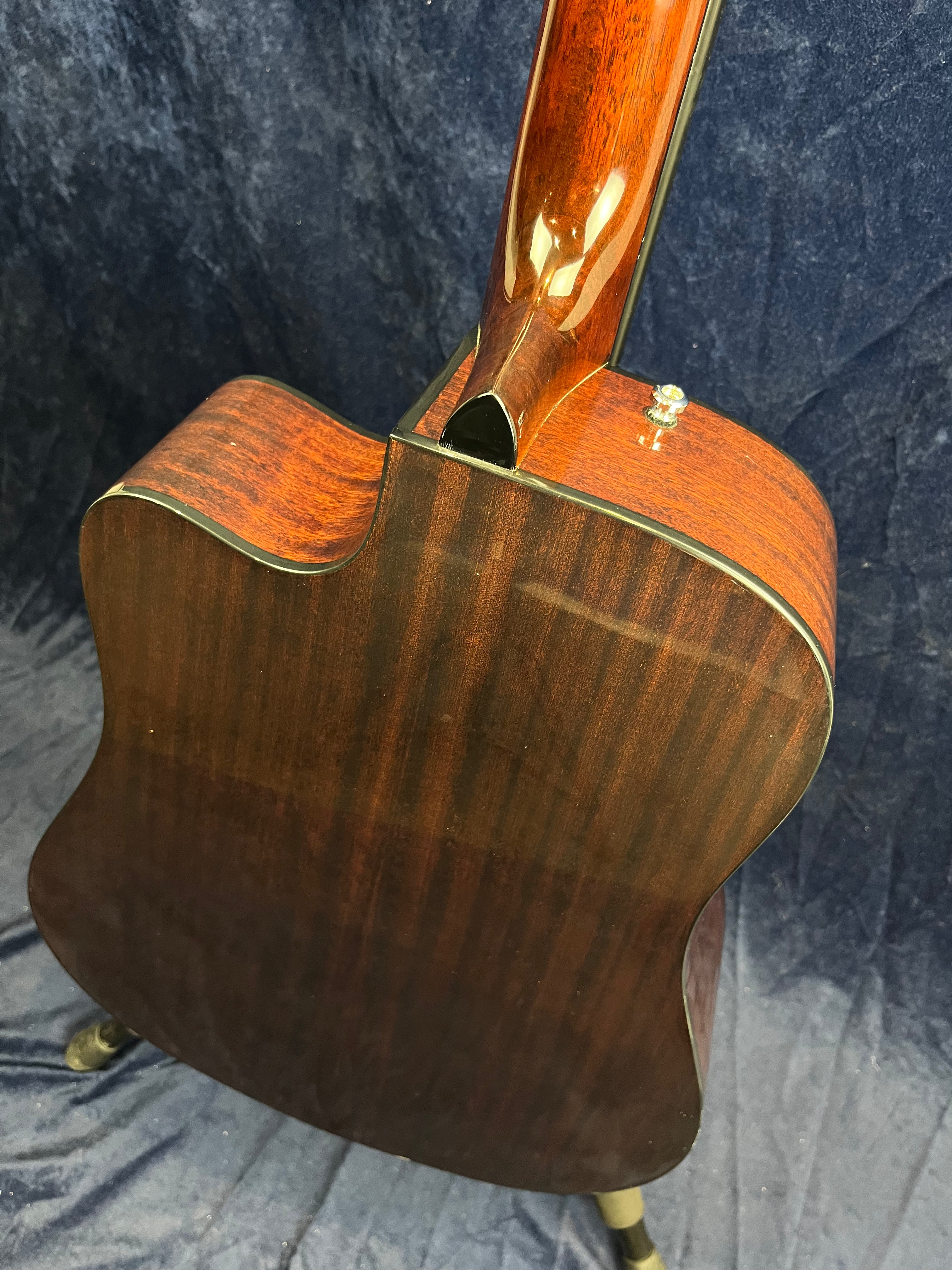 Glossy dark wood acoustic guitar back and neck with a cutaway design, viewed from behind; small strap button visible near the neck joint.