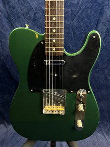 Green electric guitar with a black pickguard, chrome bridge and control plate, two knobs, and visible wear above the pickguard.