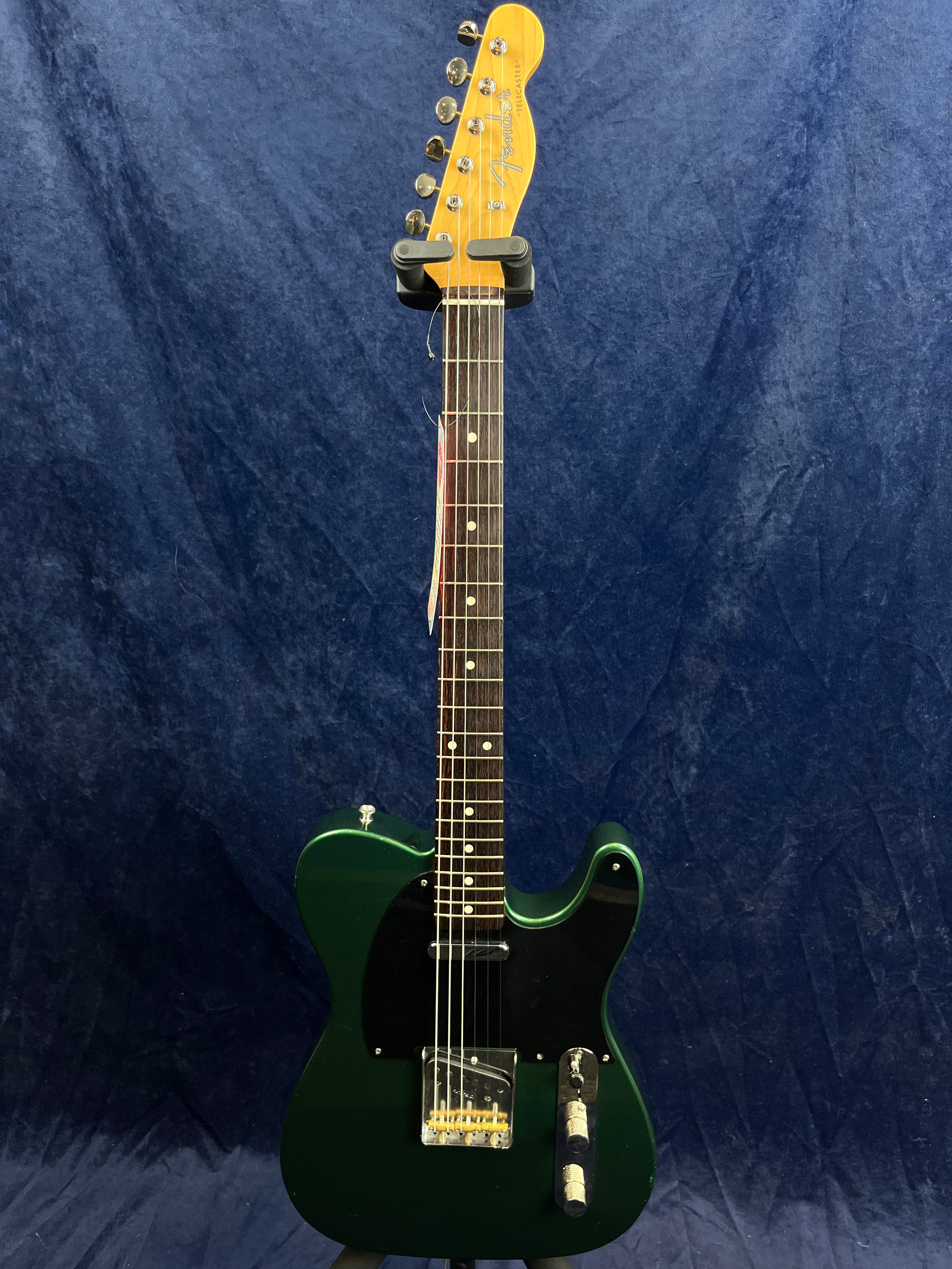 Green electric guitar with a single-cutaway body, black pickguard, two pickups, and chrome hardware, displayed vertically against a blue background.
