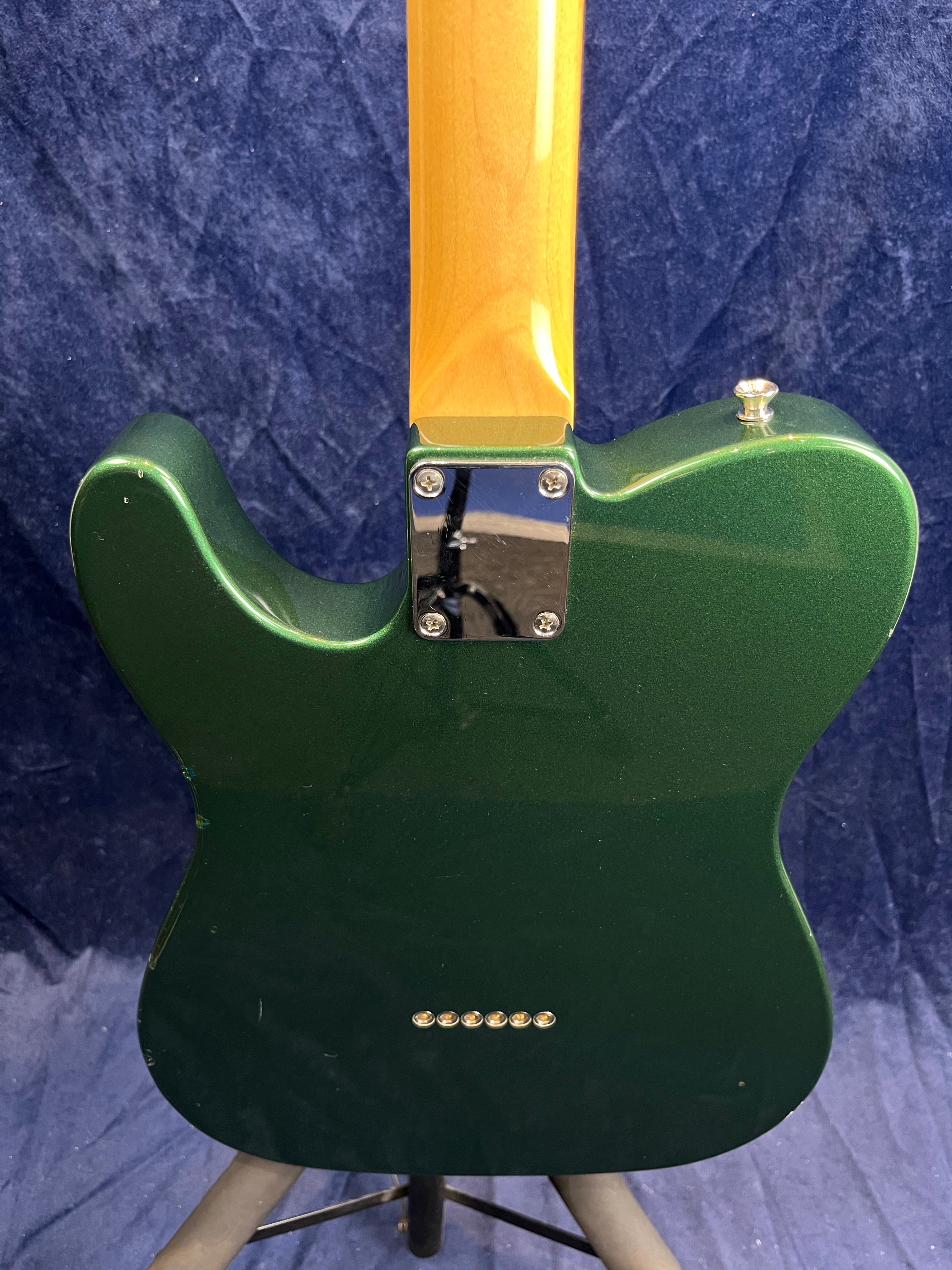 Green electric guitar body and maple neck, viewed from the back; six string ferrules and a metal neck plate with four screws are visible.
