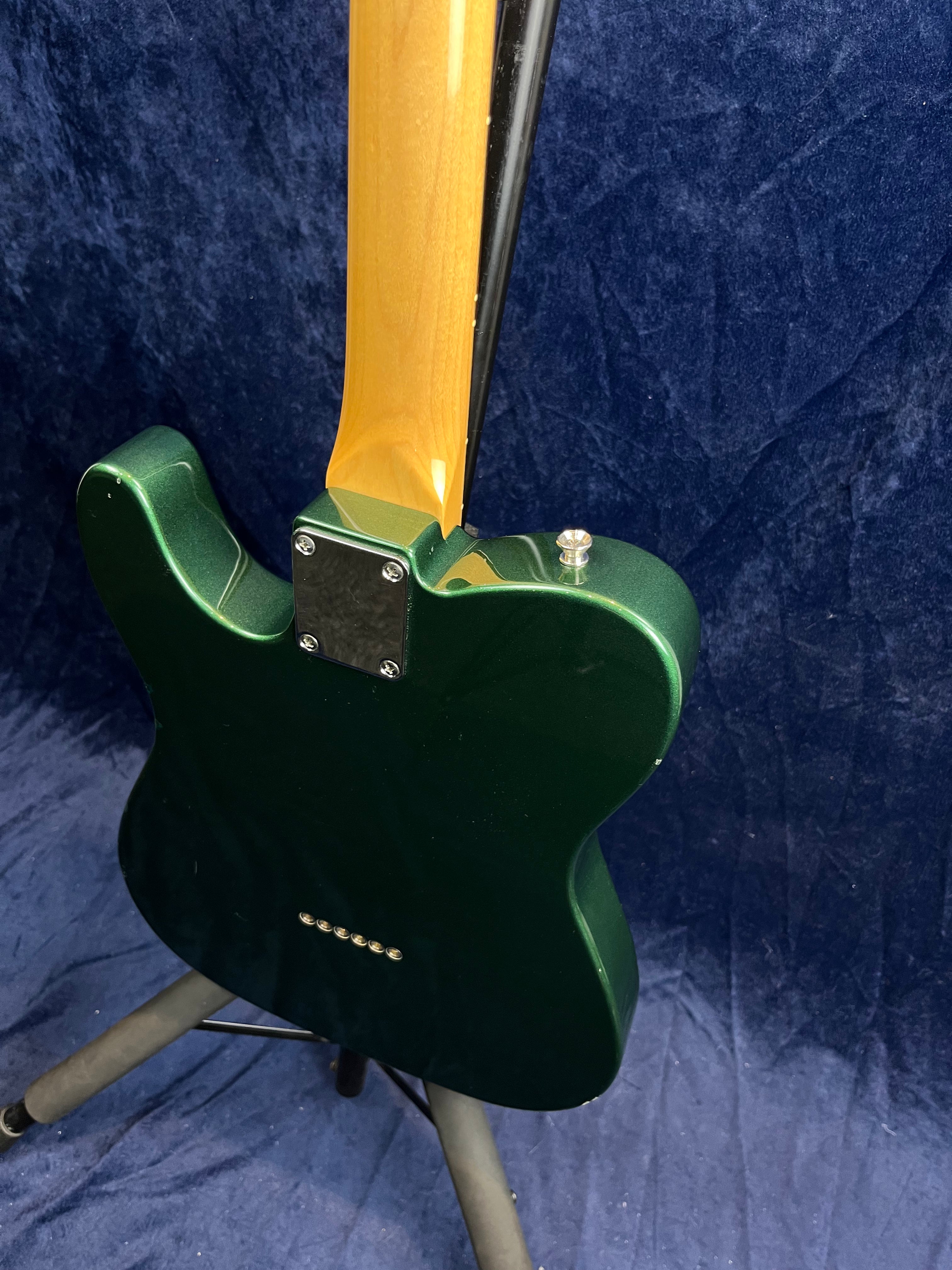 Green electric guitar on a stand, shown from the back with a natural wood neck and chrome neck plate, against a dark blue textured background.