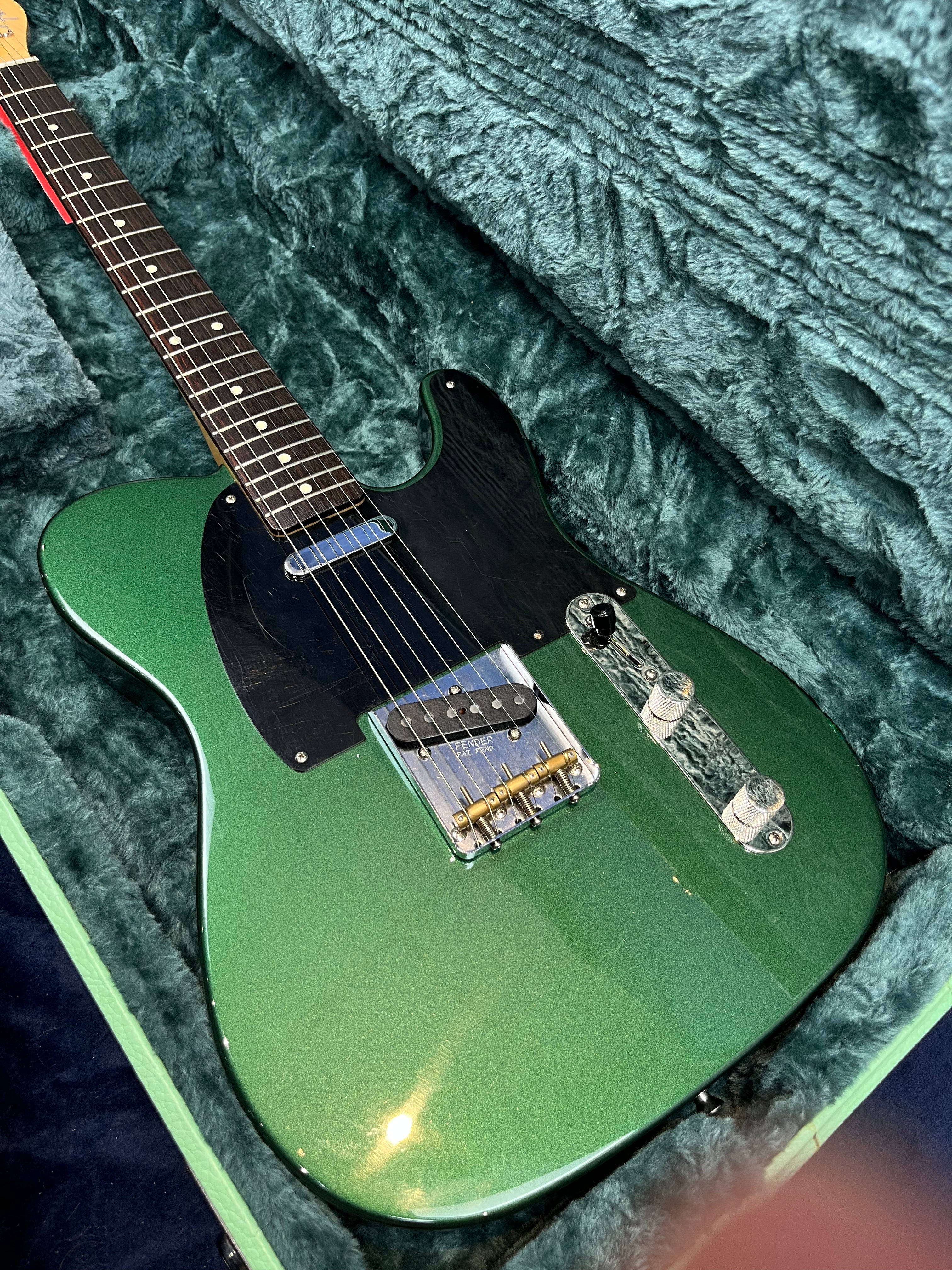 Green electric guitar with a black pickguard, chrome bridge, and control knobs, resting in a plush green case.