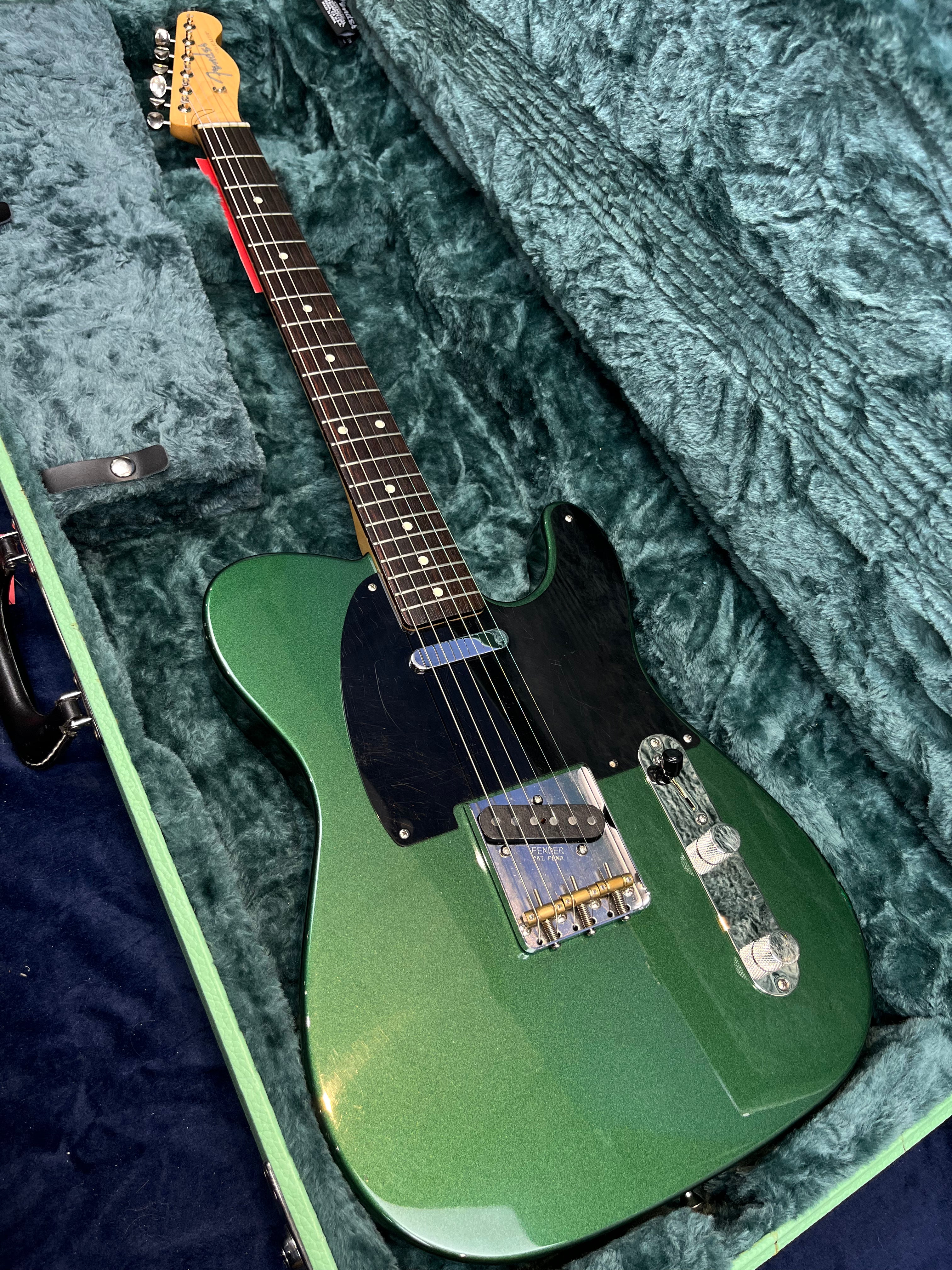 Metallic green electric guitar with black pickguard and chrome hardware resting inside a plush, green-lined hard case.