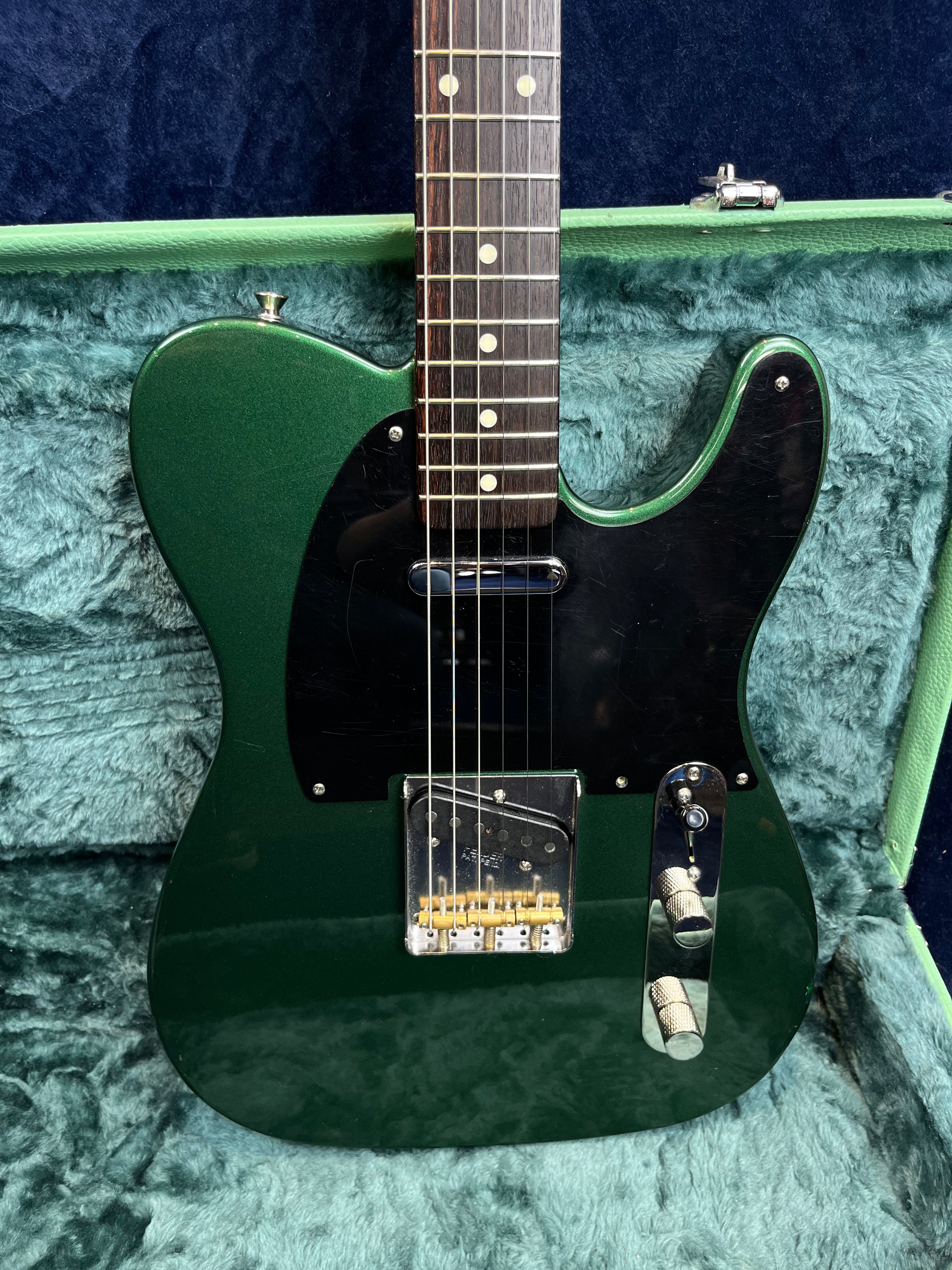 Green electric guitar with a black pickguard, chrome knobs, and a rosewood fretboard, resting in a plush blue-green case.