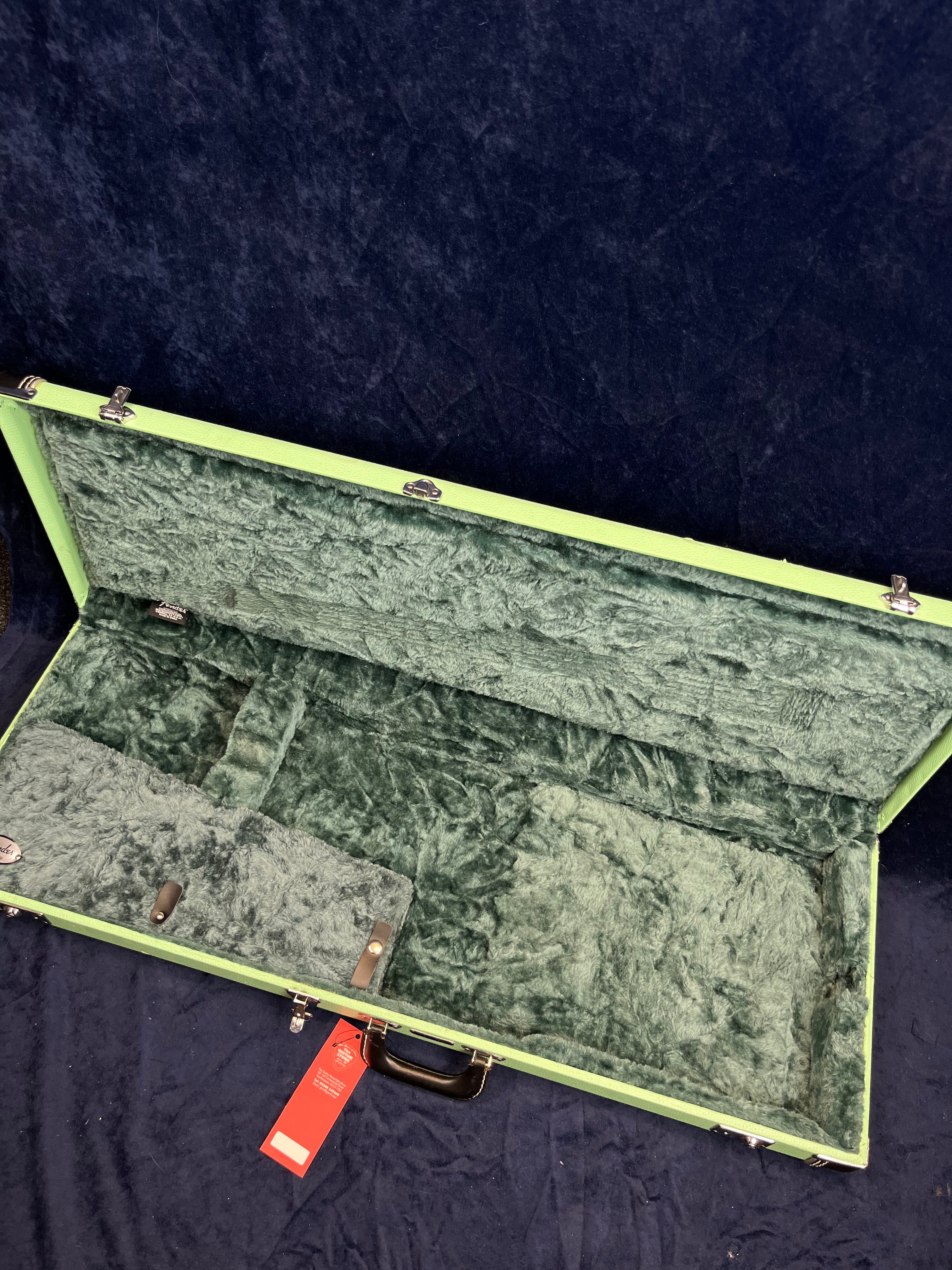 Empty green electric guitar case with plush dark green interior lining, accessory compartment, and black carrying handle.