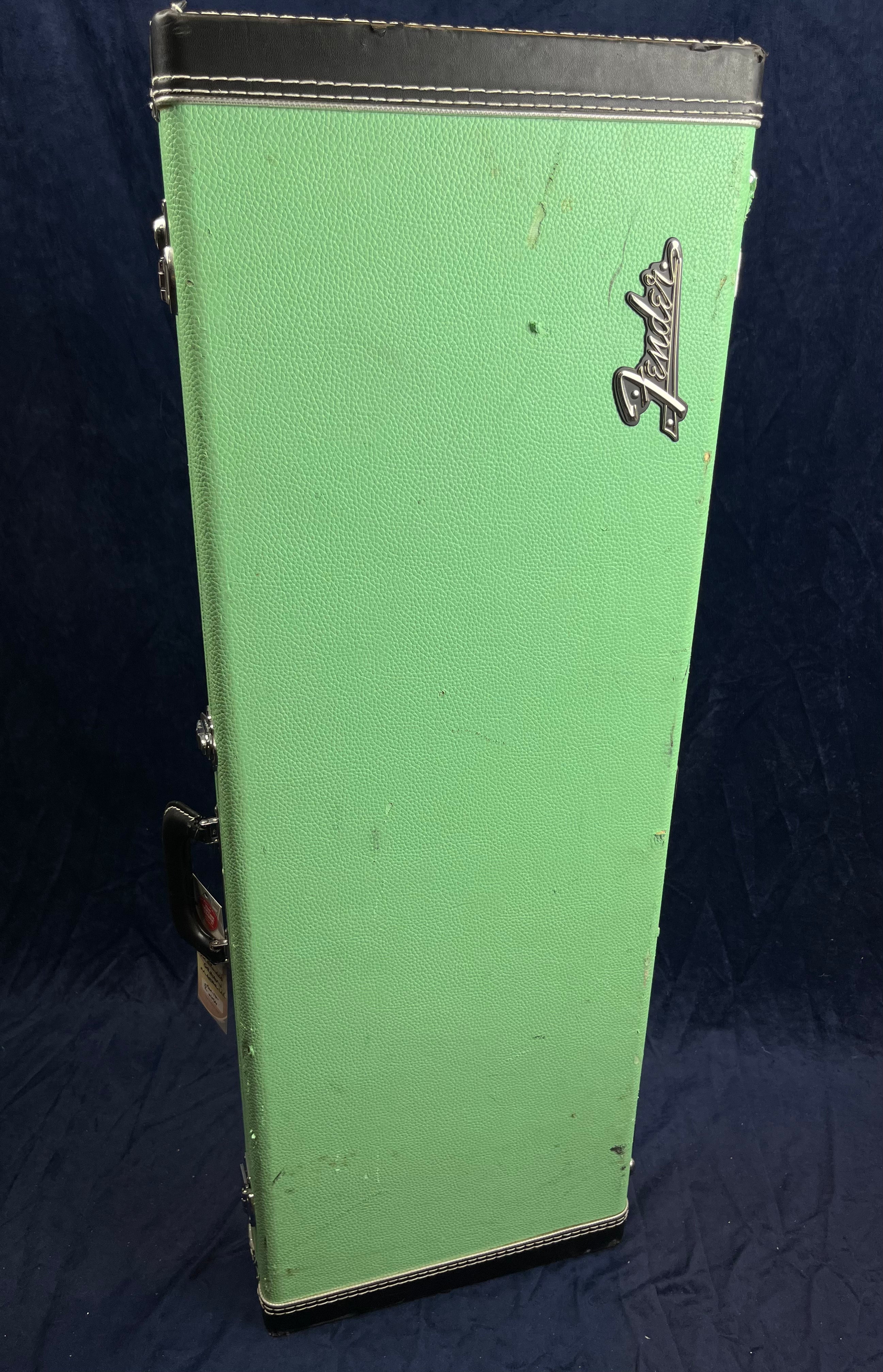 Green Fender electric guitar case standing upright with a black handle and minor scuffs visible on the surface.