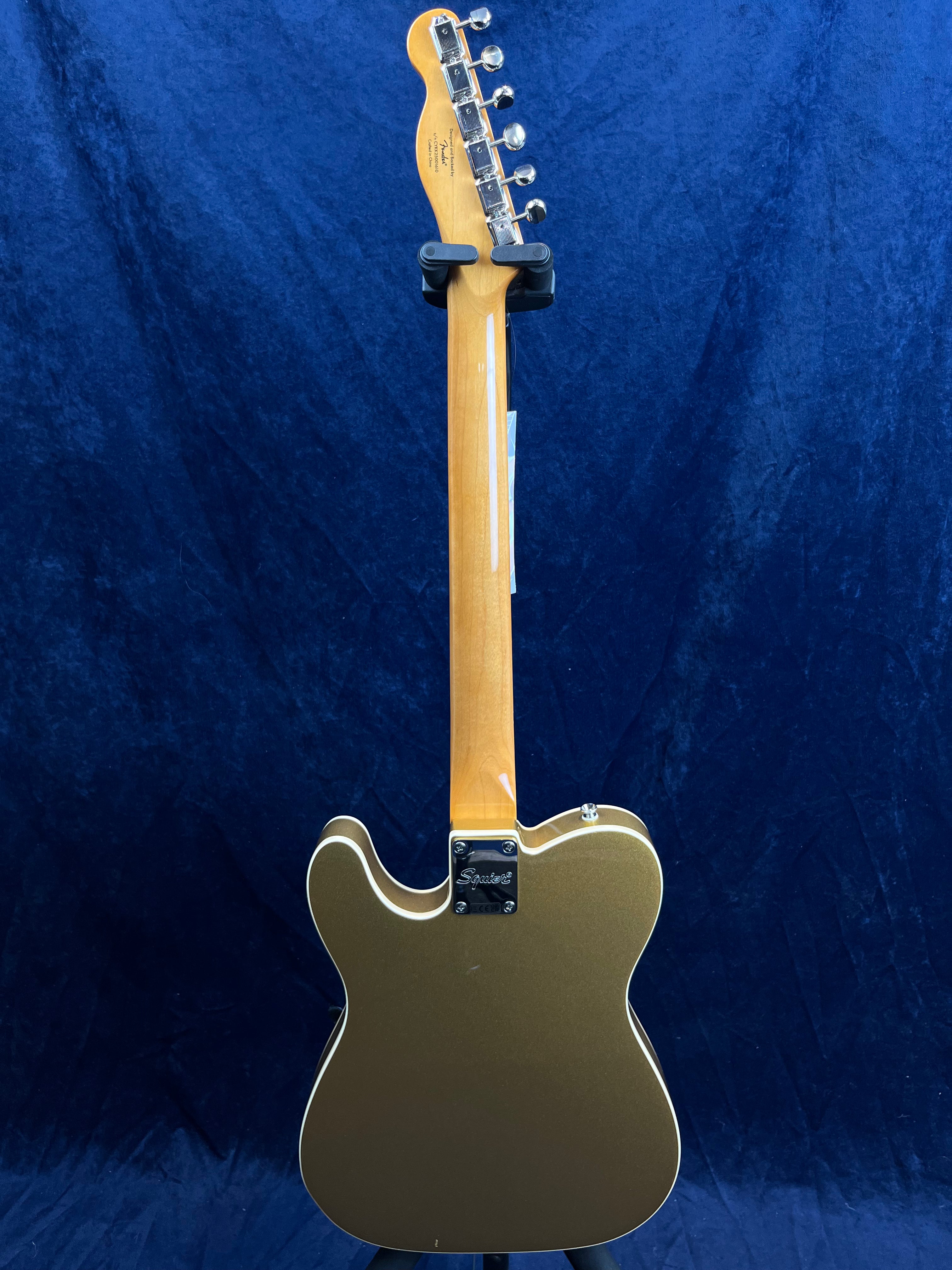 Gold Squier electric guitar shown from the back, displaying a light wood neck, silver tuning pegs, and a contoured metallic gold body with white binding.