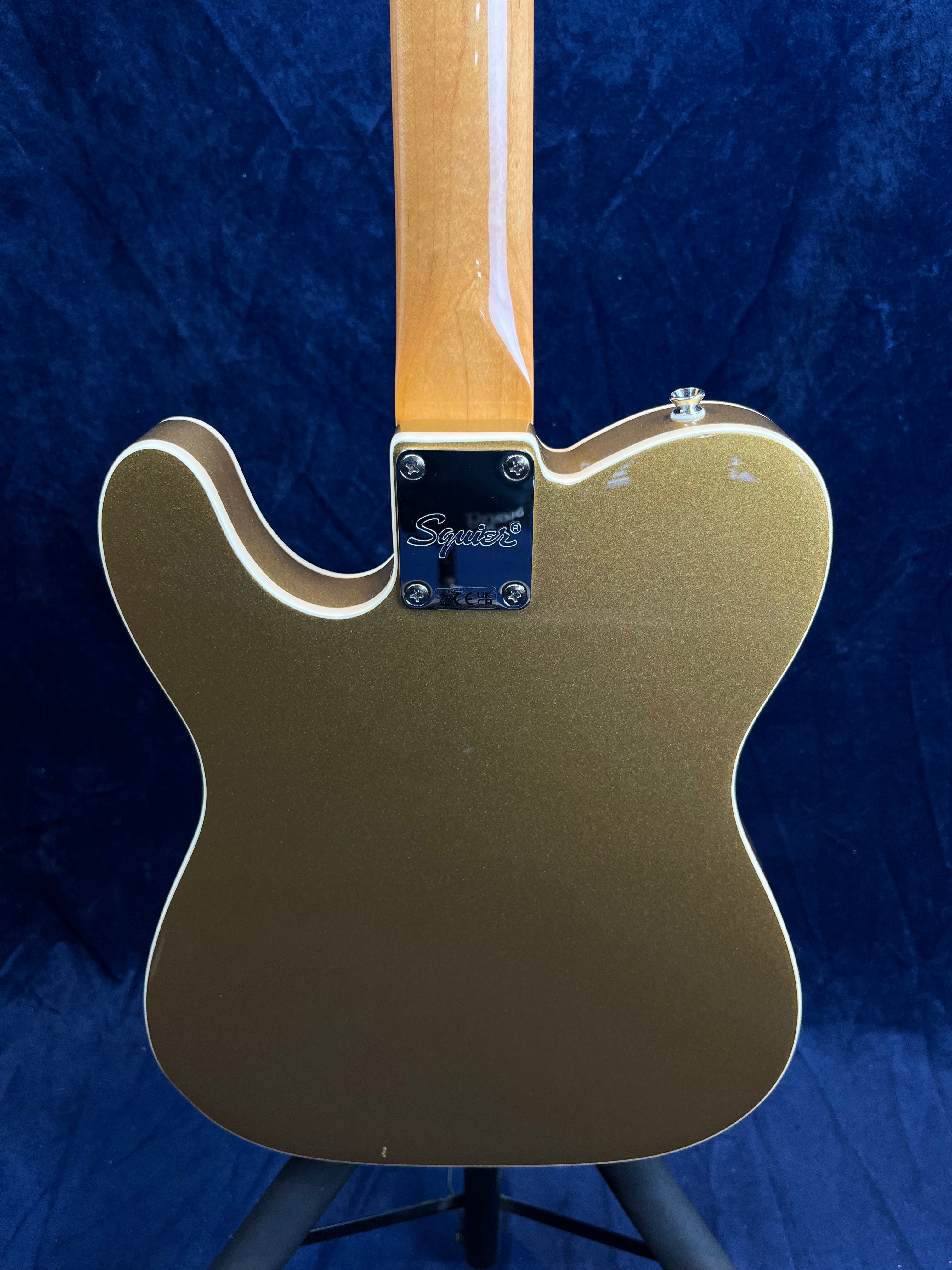 Gold electric guitar, viewed from the back, showing a glossy maple neck and the Squier brand plate at the neck joint.