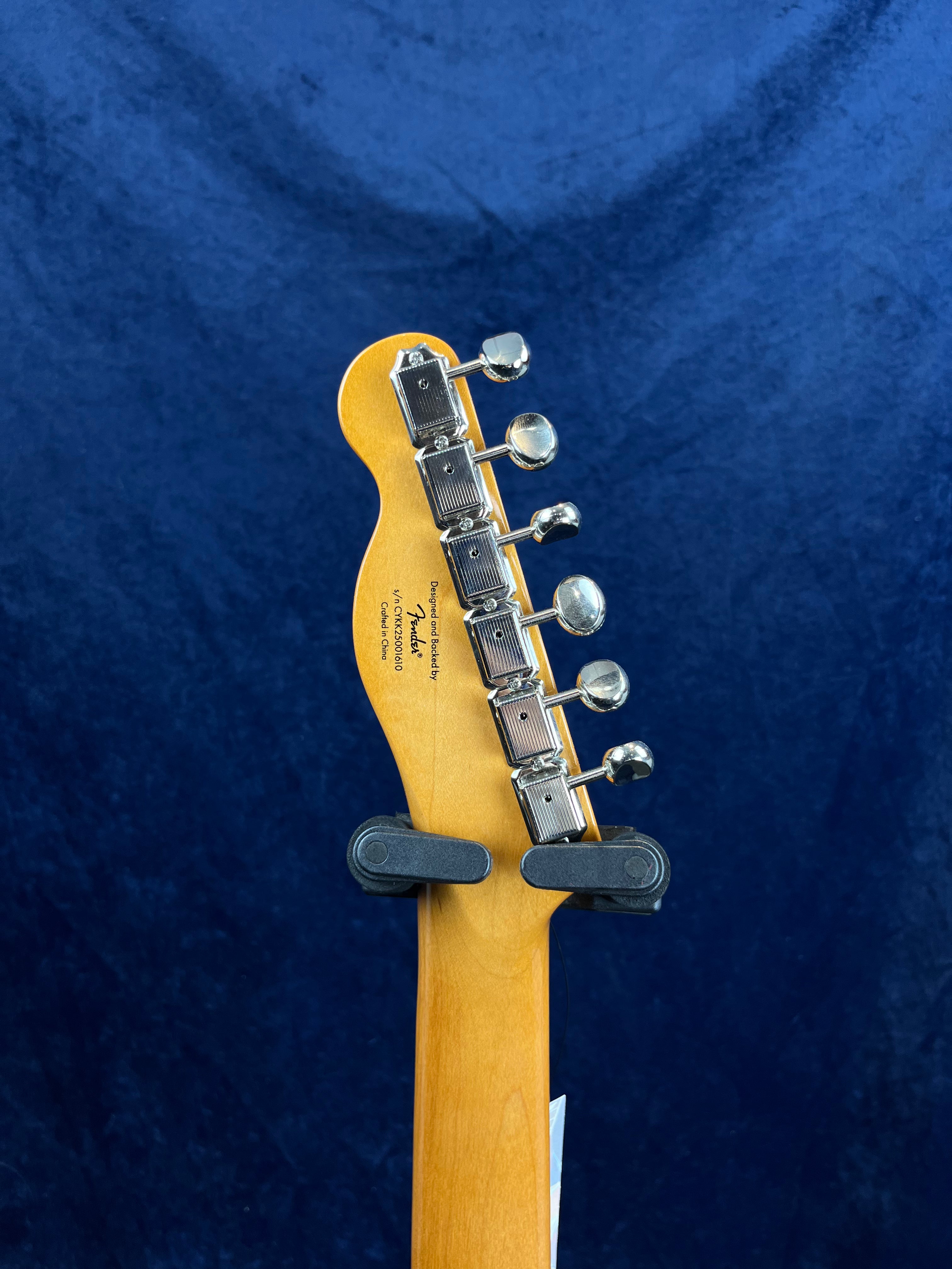 The back of a Fender electric guitar headstock with six metal tuning pegs, shown against a dark blue background.