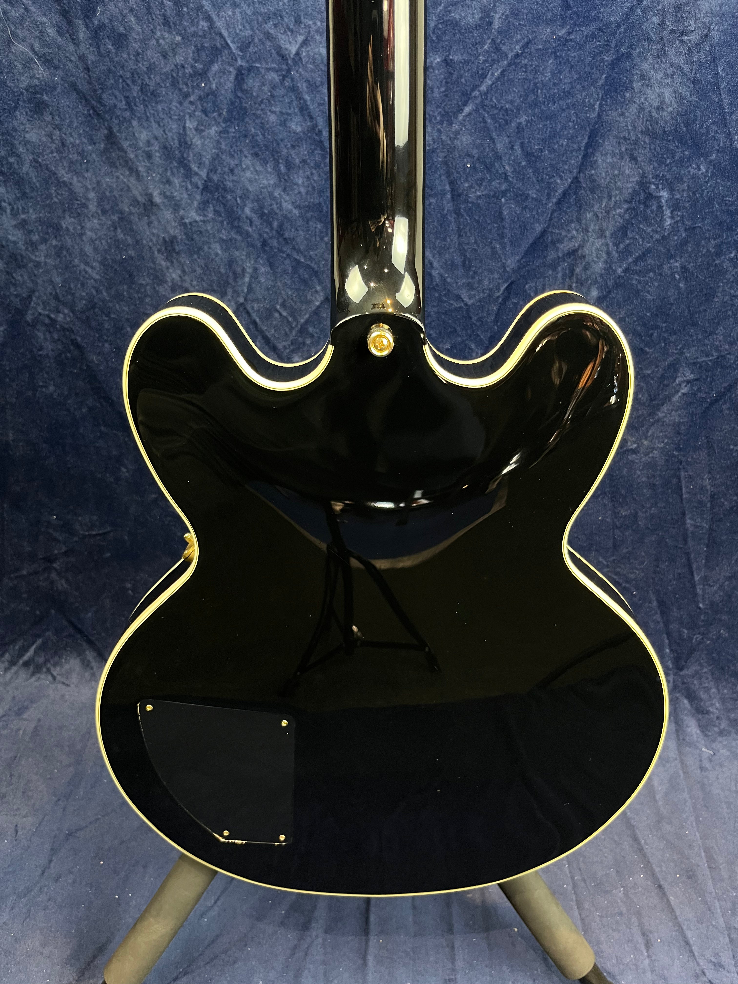 Black semi-hollow electric guitar shown from the back, cream binding around the body edges, with a control cavity cover and gold strap button.