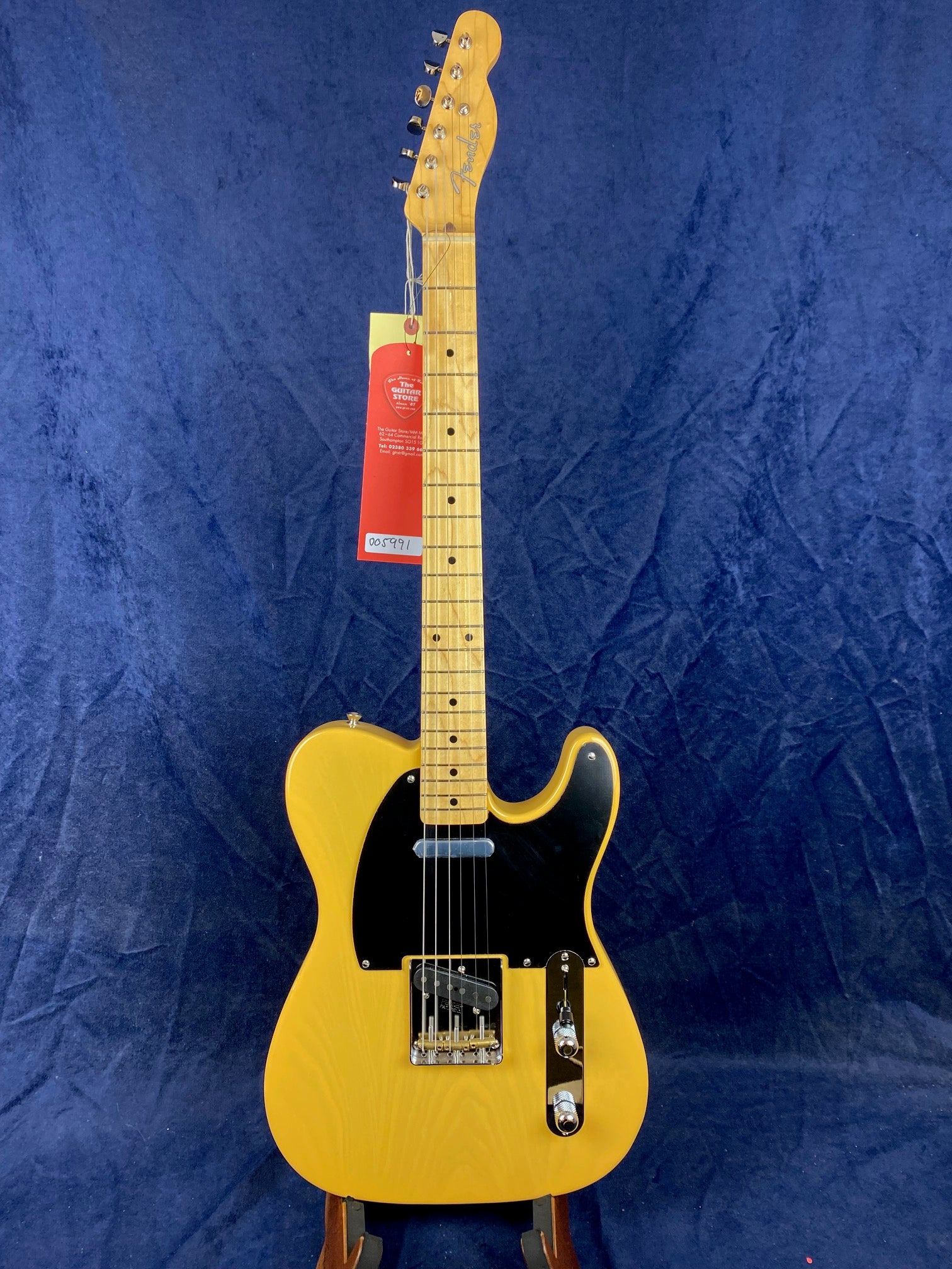 Yellow Fender electric guitar with a black pickguard, maple neck, and chrome hardware, displayed upright against a blue background.