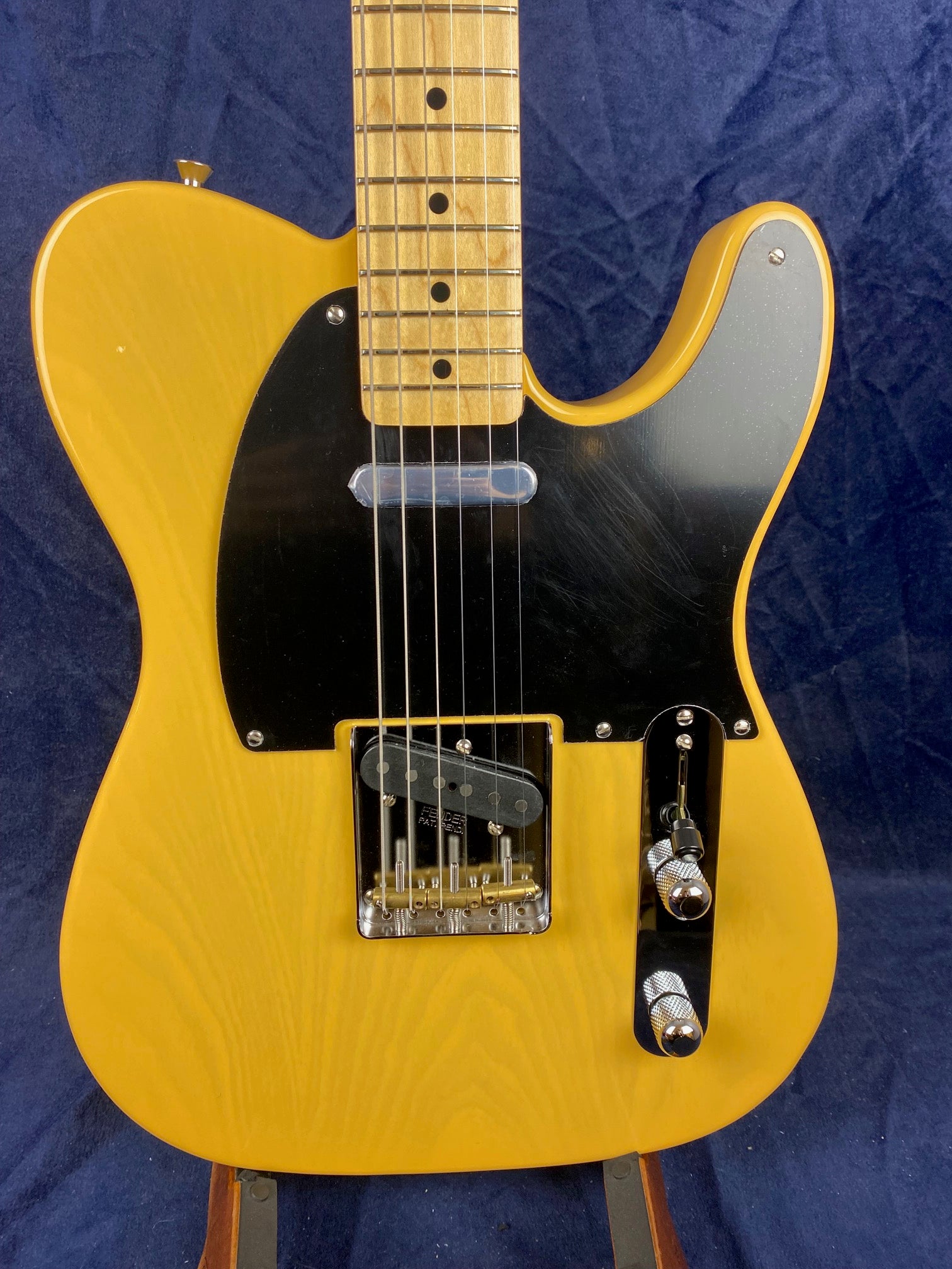 Yellow Fender electric guitar with a black pickguard, chrome hardware, and maple fretboard, shown from the body up to part of the neck.