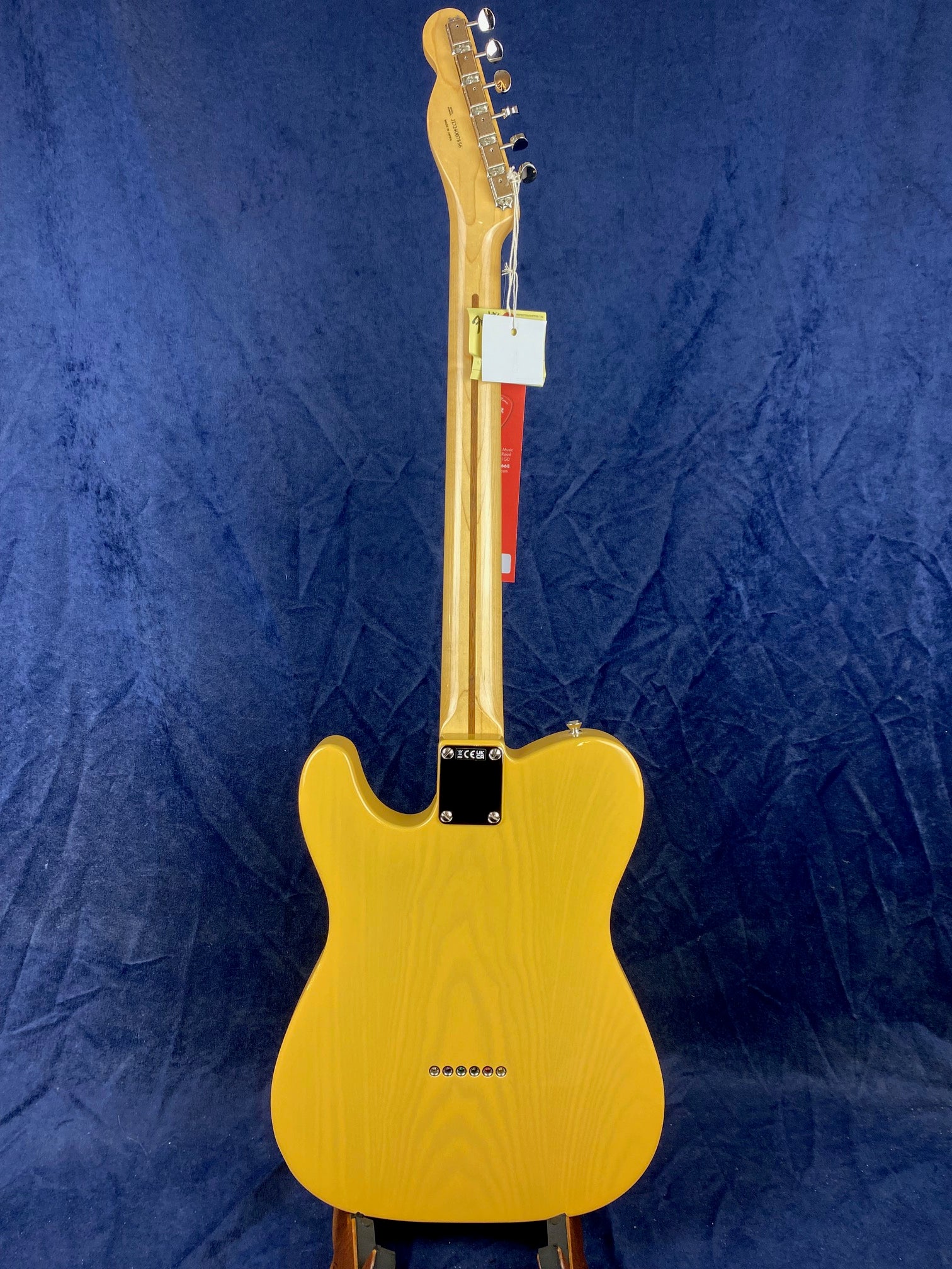 Yellow Fender electric guitar shown from the back, displaying a wooden neck, six tuning pegs, and string ferrules across the body bottom.