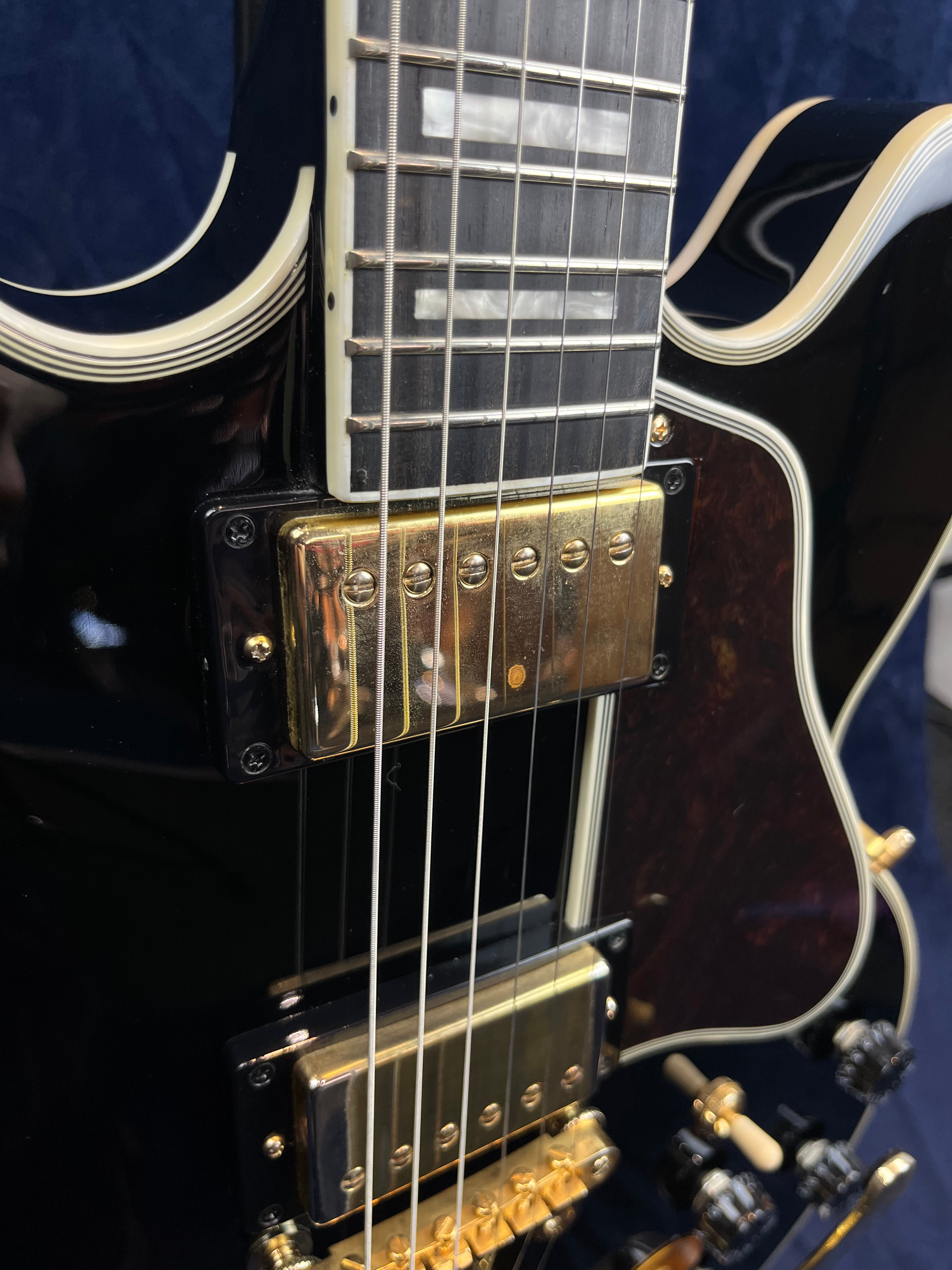 Close-up of a black electric guitar showing gold humbucker pickups, six strings, and cream binding along the body and neck edges.
