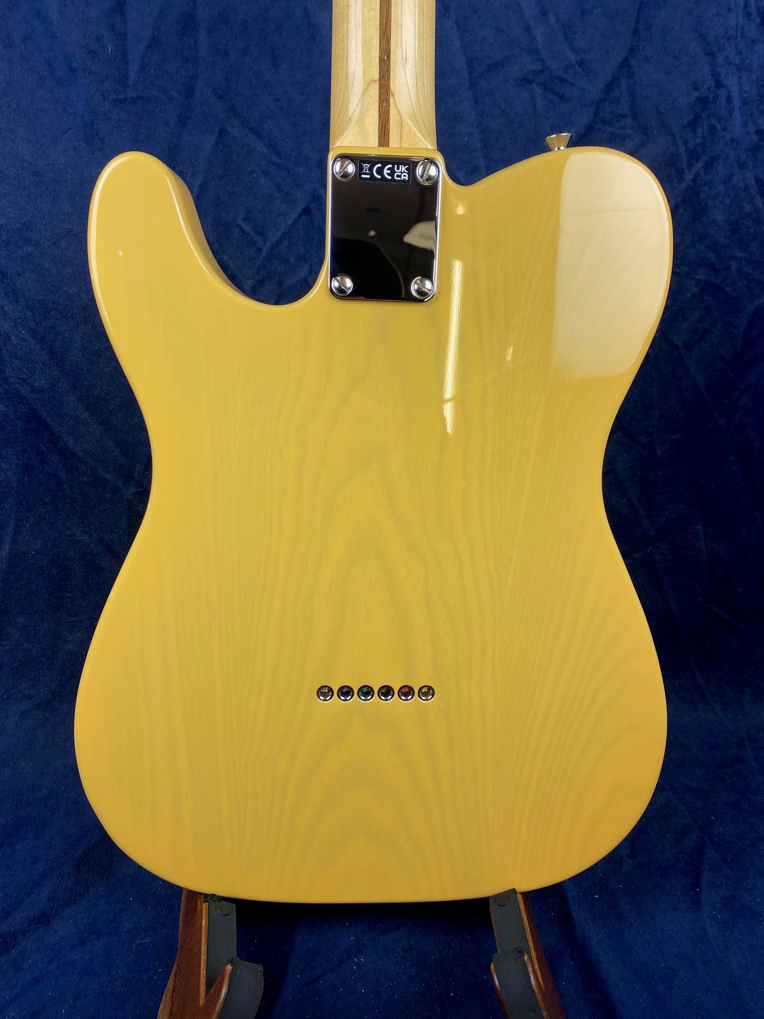 Yellow Fender electric guitar body seen from the back, showing six string ferrules and a metal neck plate with certification marks.