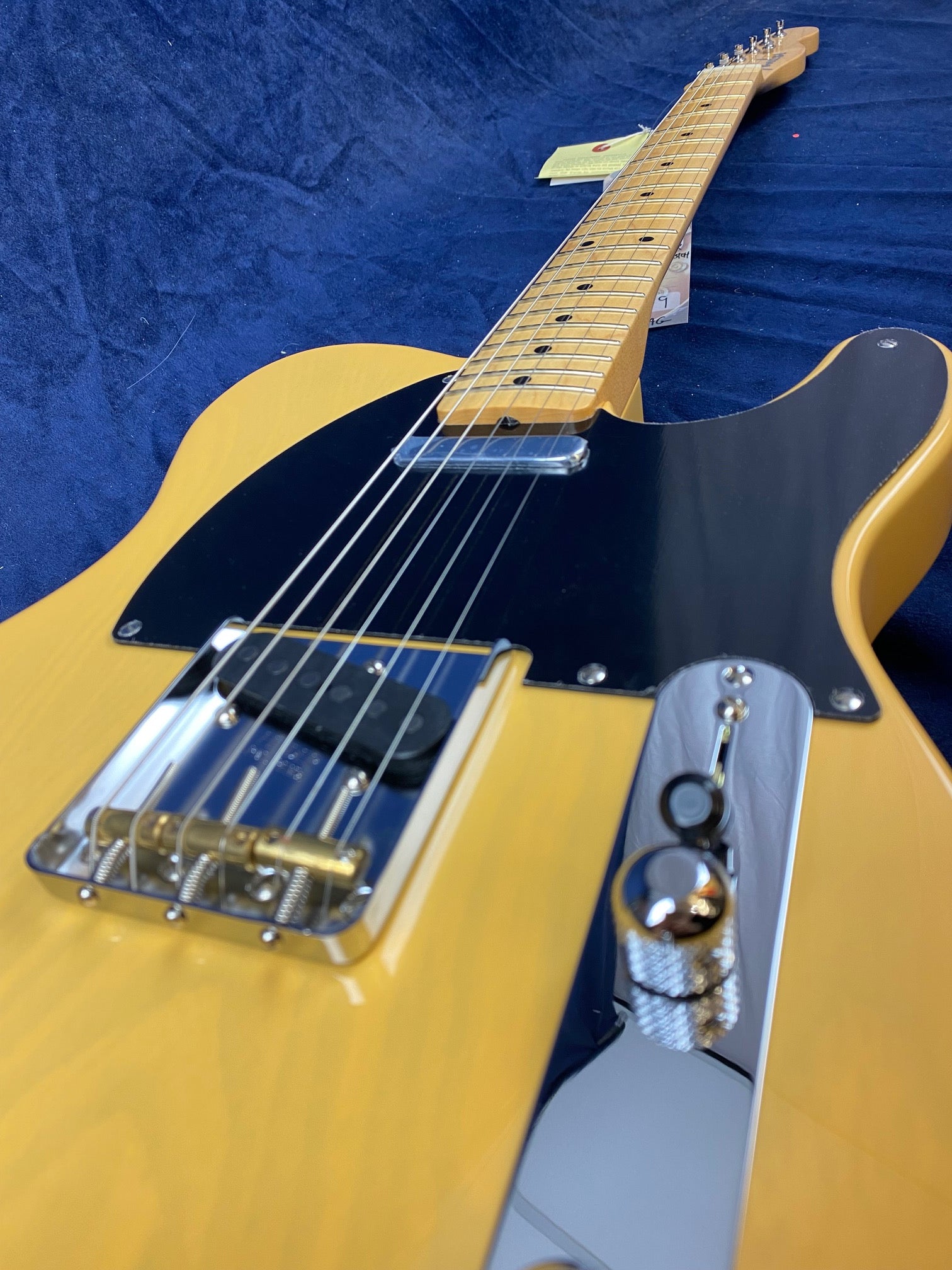 Yellow Fender electric guitar with a black pickguard, maple neck, silver hardware, and six strings, lying on a dark blue fabric background.
