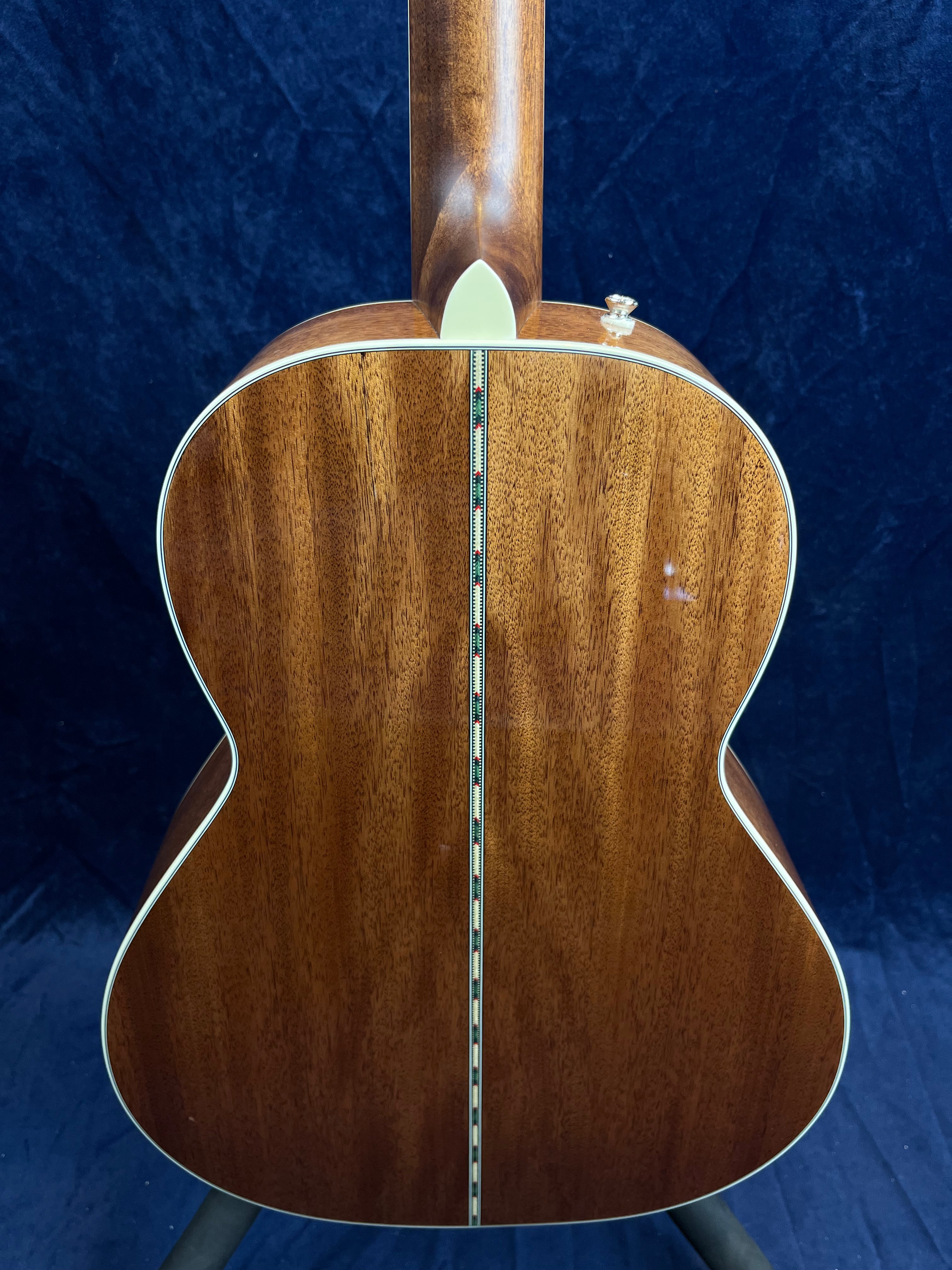 The acoustic guitar’s back is made of polished brown wood with a decorative inlaid strip running vertically down the center and light binding along the edges.