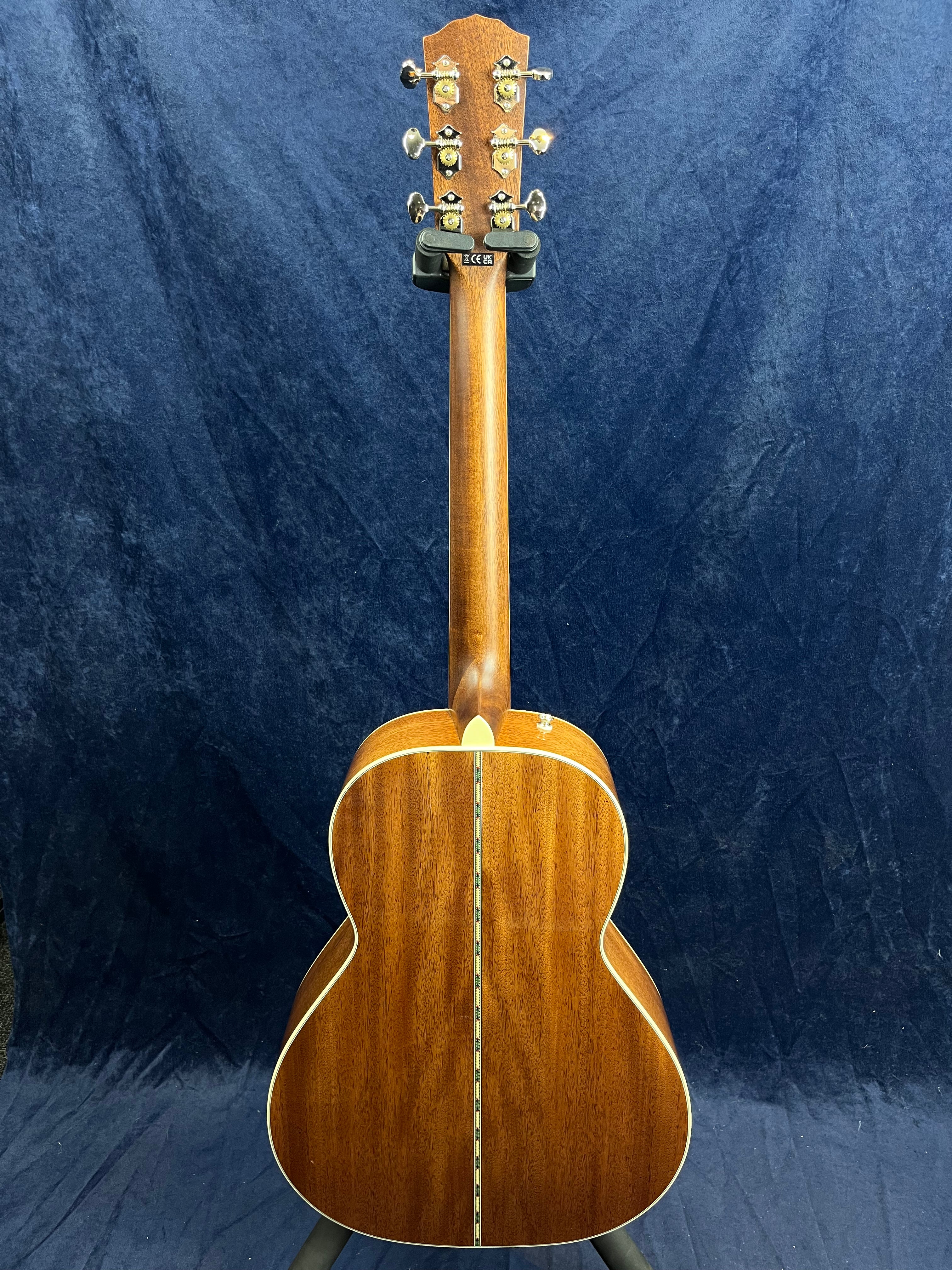 Acoustic guitar shown from the back, featuring a rich brown wood finish with a decorative center seam and gold tuning pegs on the headstock.