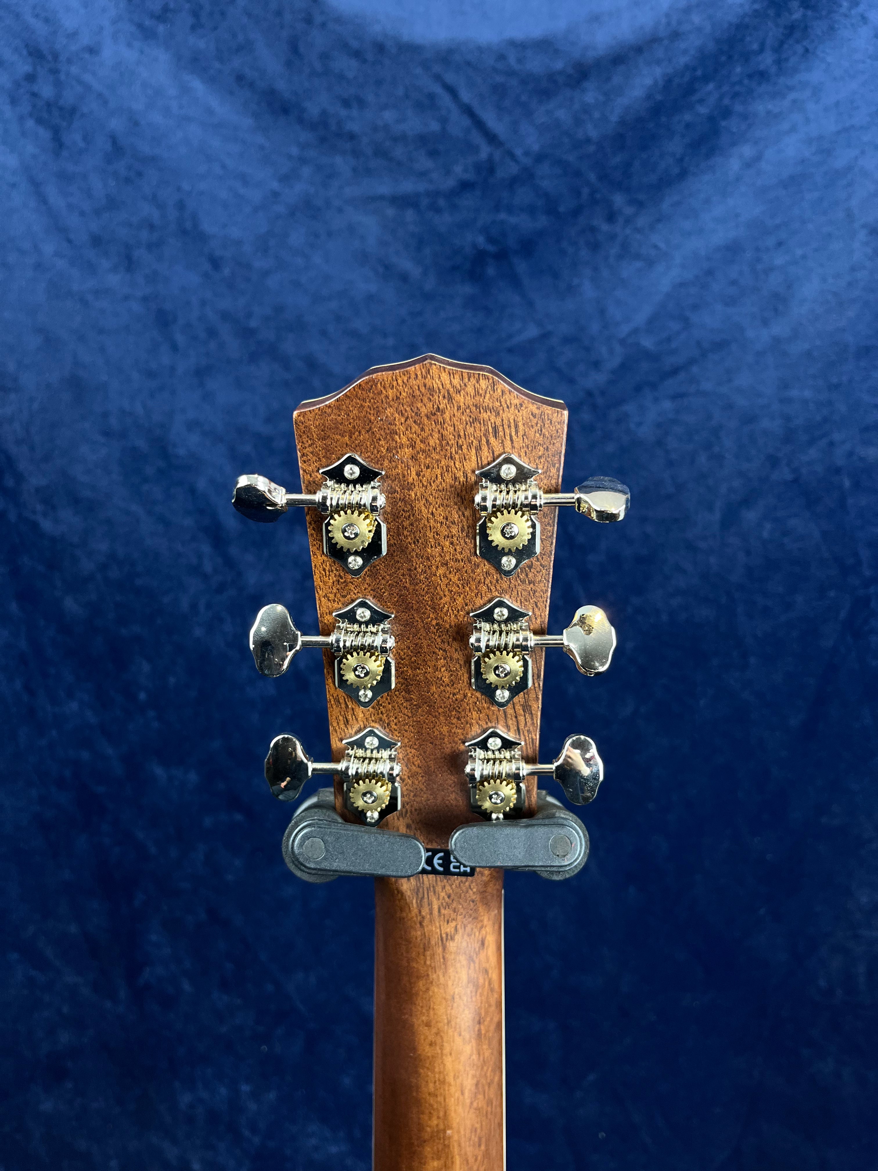 Back of an acoustic guitar headstock showing six chrome tuning pegs, set against a dark blue textured background.