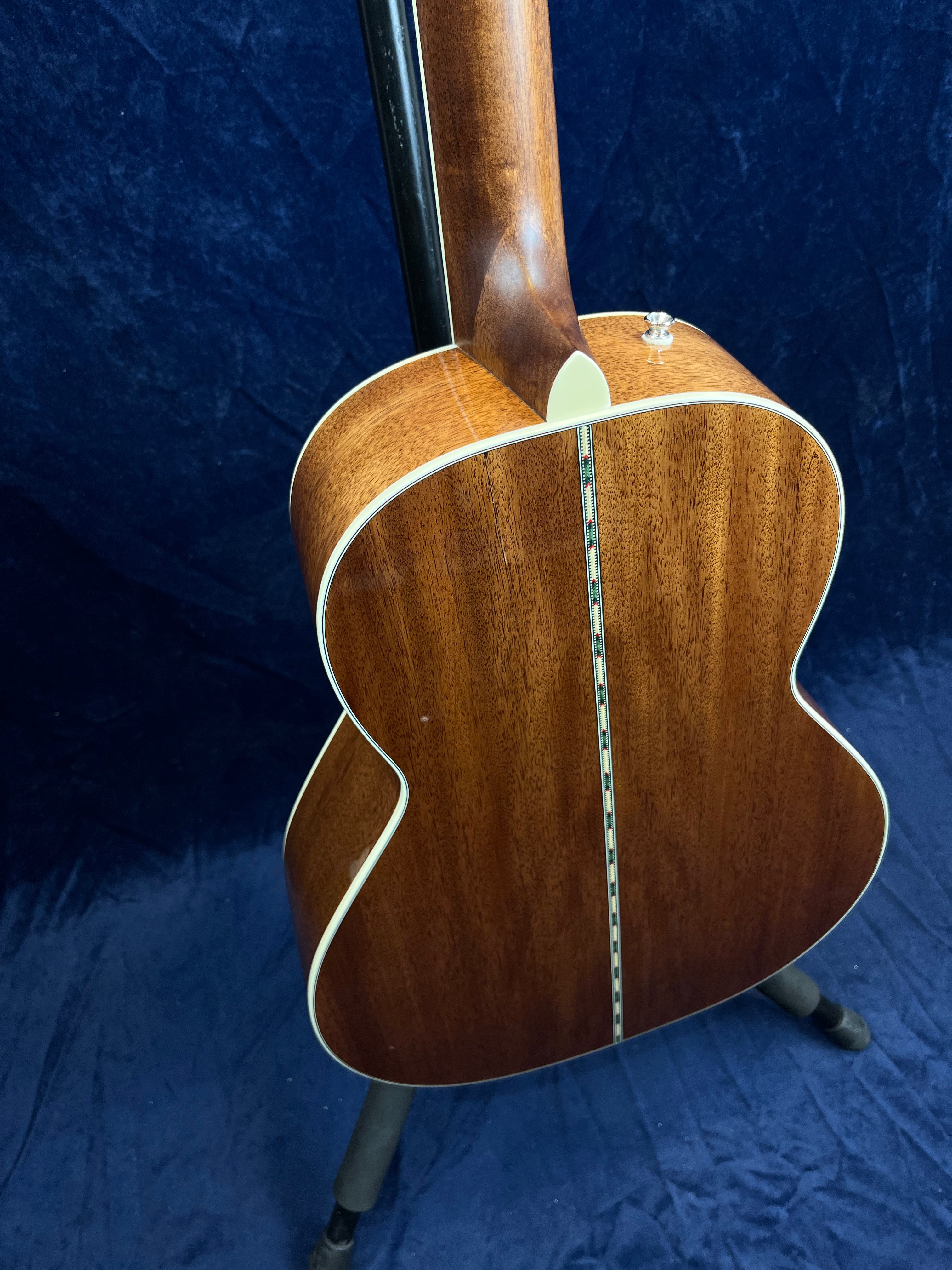 Brown acoustic guitar with a glossy wood back, cream-colored edges, and a decorative inlay strip running down the center.