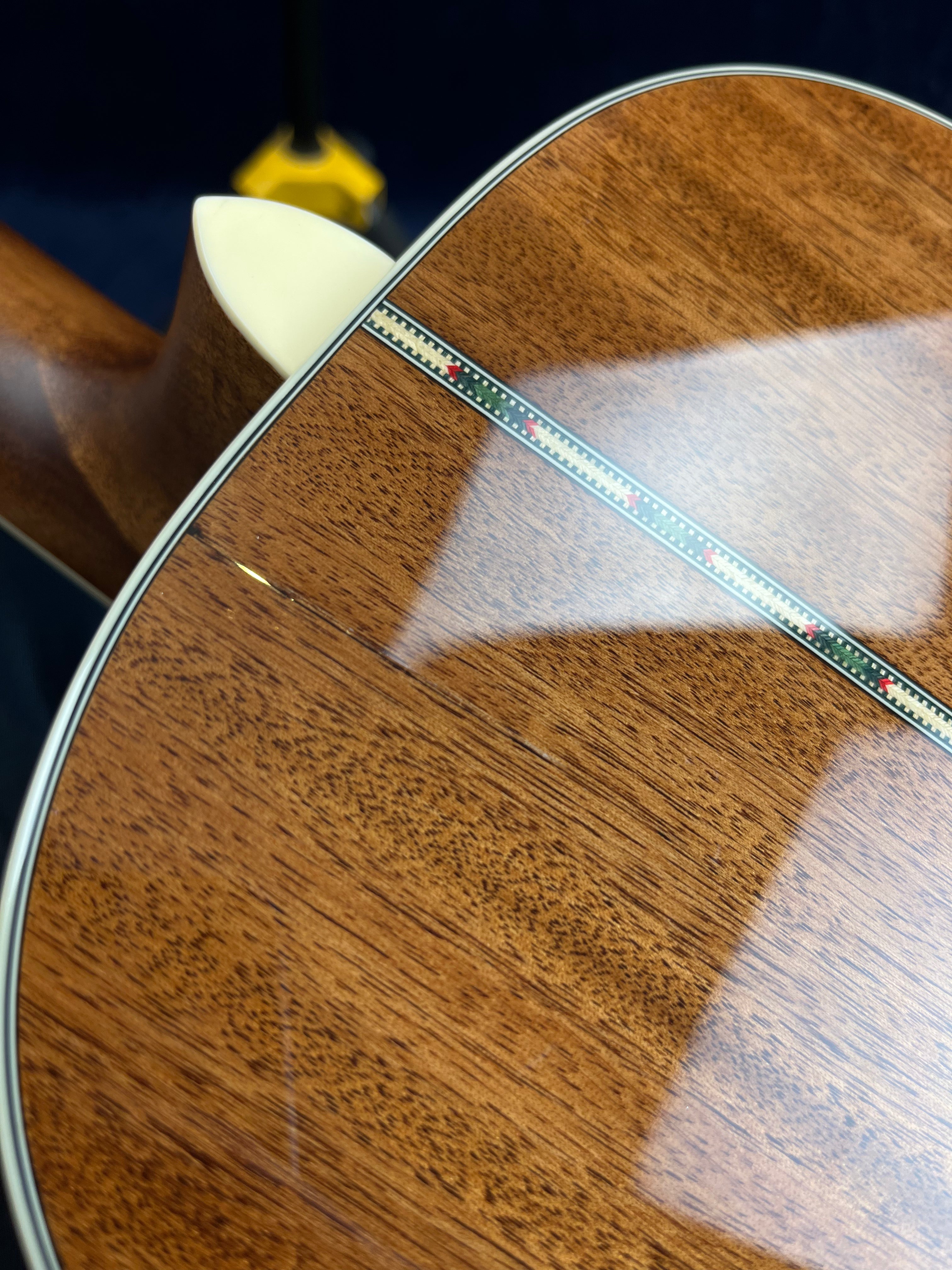 Glossy wooden acoustic guitar back with a decorative center strip and cream binding at the neck joint, showing fine wood grain and smooth finish.
