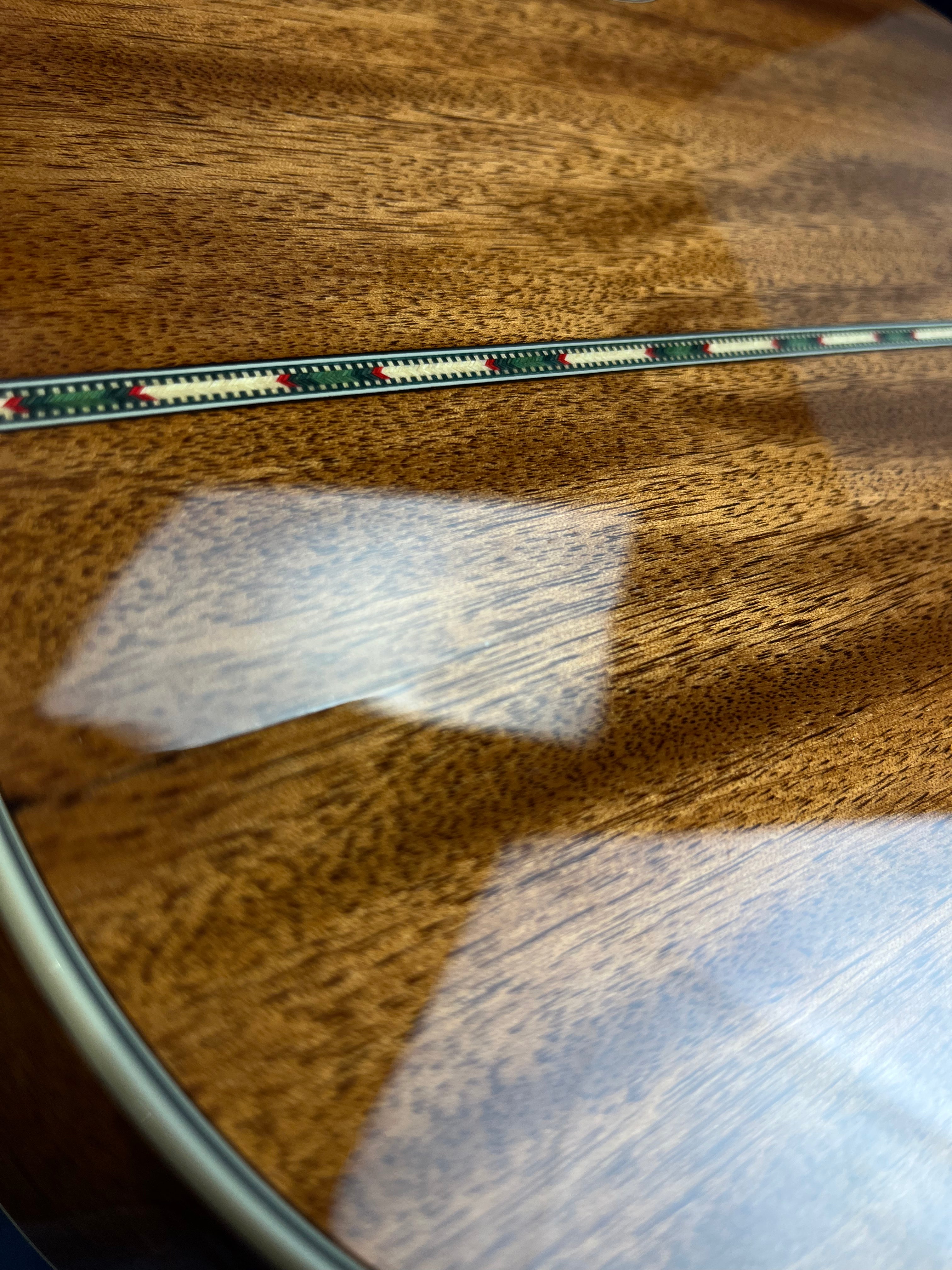 Glossy wooden acoustic guitar back with a narrow decorative inlay strip running down the center, featuring green, red, and cream patterns.