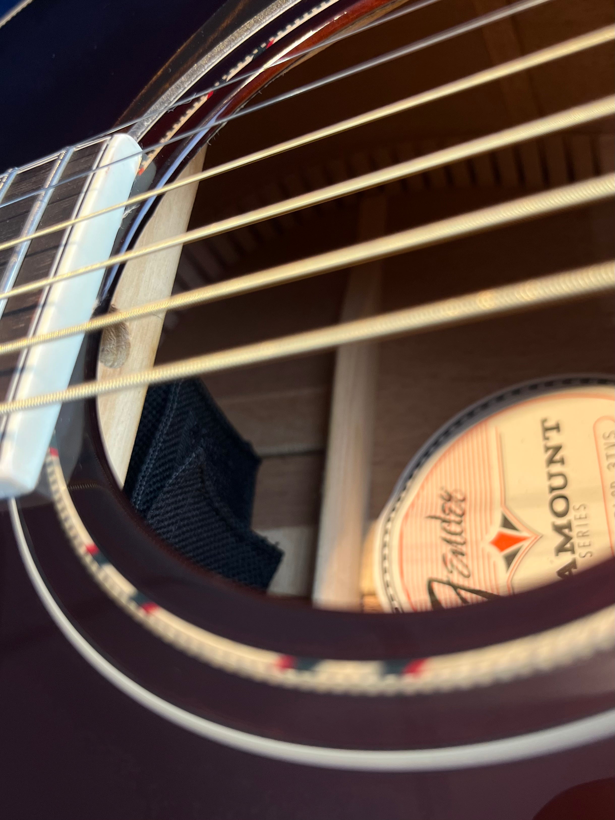 Close-up view of an acoustic guitar’s body, showing strings, the sound hole, internal bracing, and a partially visible Paramount Series Fender label inside.