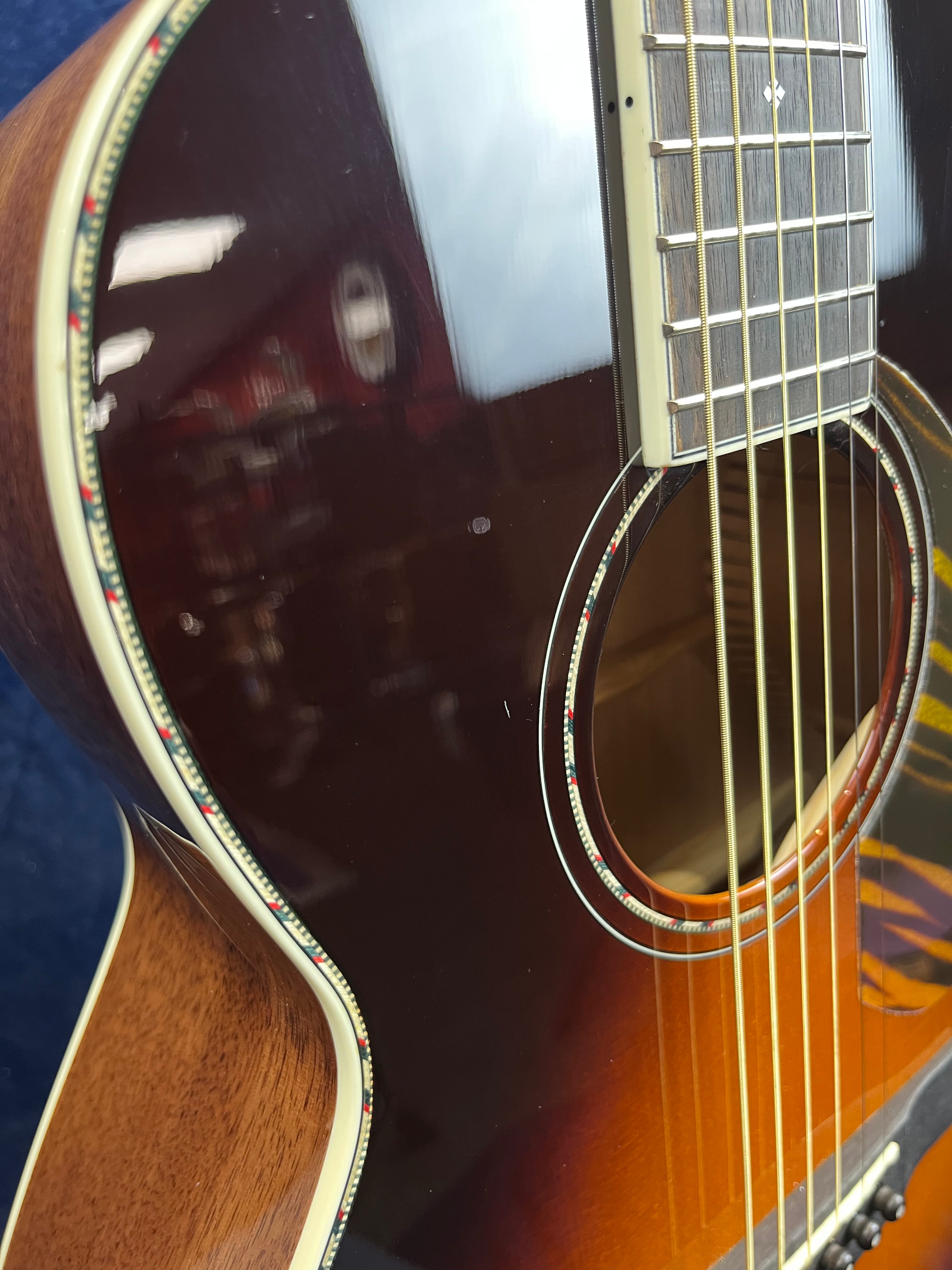 Close-up of an acoustic guitar showing glossy sunburst finish, detailed rosette, and six steel strings over a wooden body with cream and patterned binding.