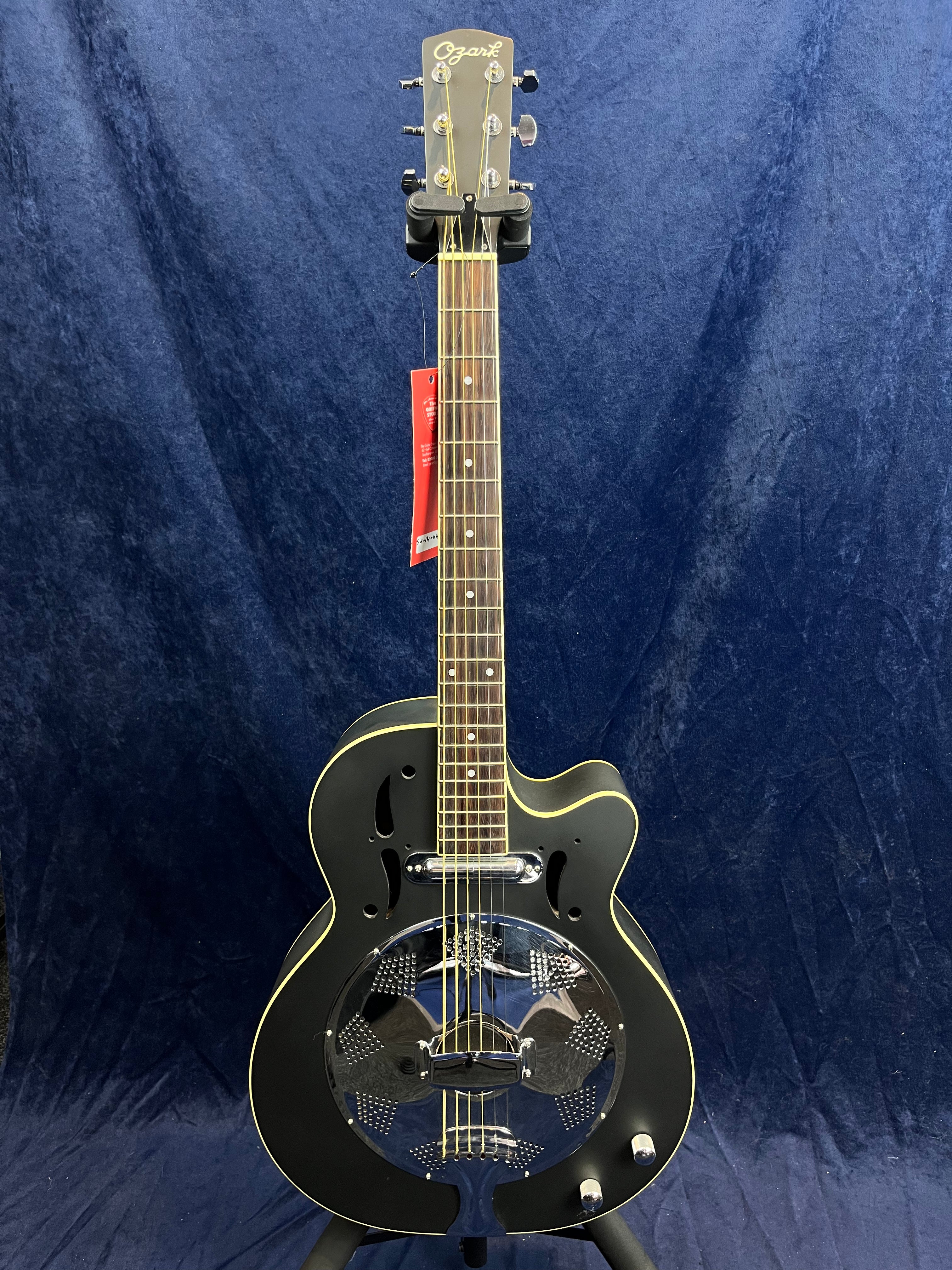 Guitare électrique de forme single cutaway, corps noir mat avec résonateur métallique circulaire argenté et deux boutons de réglage.