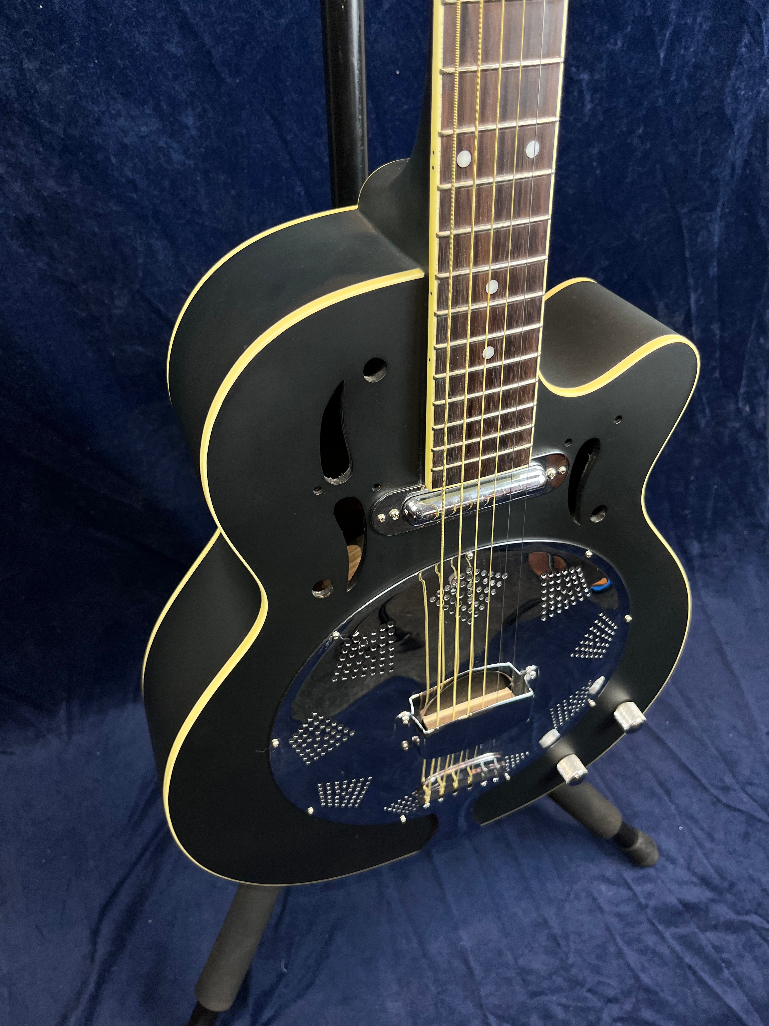 Guitare électrique noire à caisse creuse avec contour crème, plaques métalliques percées et deux boutons argentés sur la partie inférieure du corps.