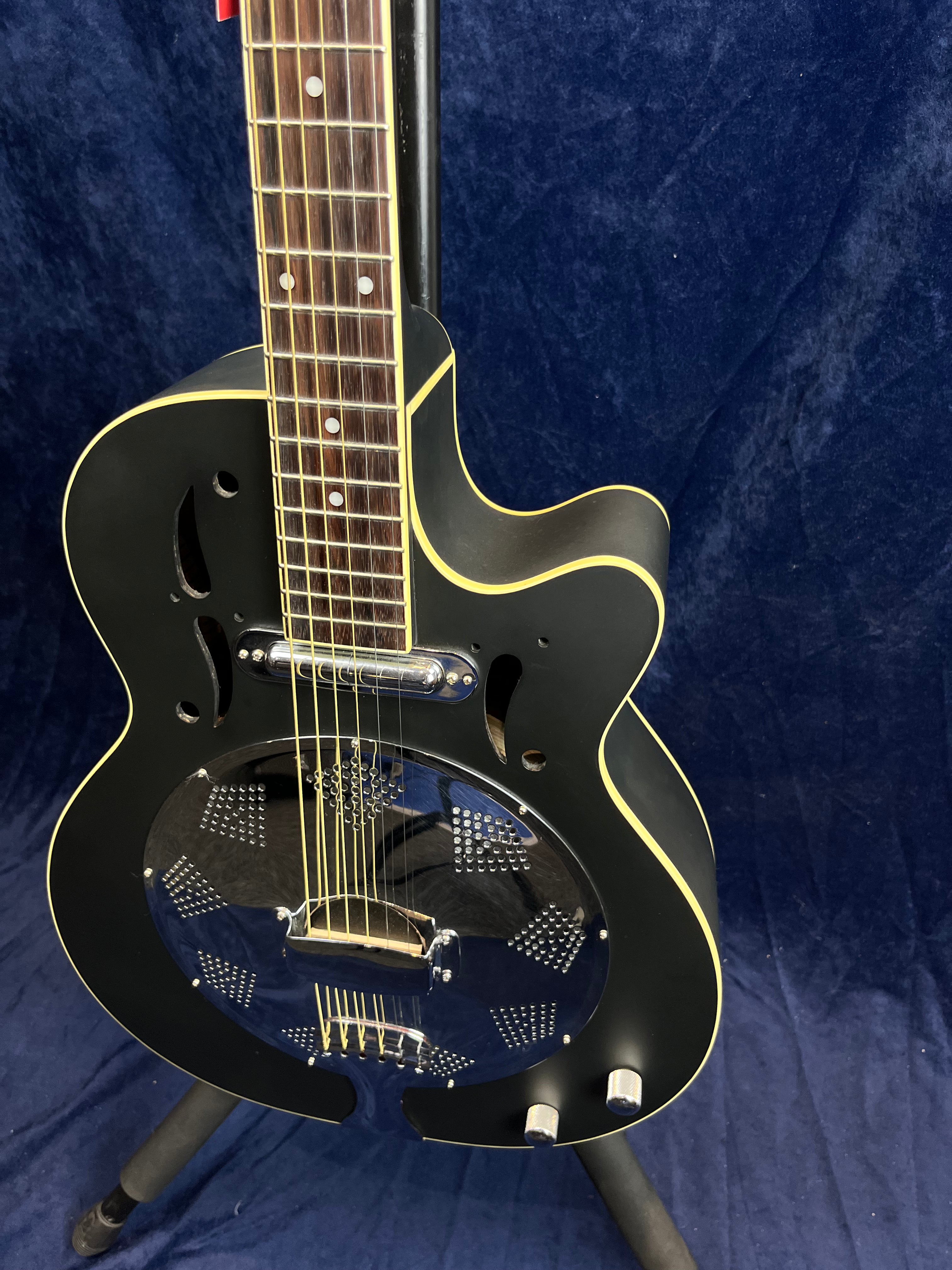 Guitare électrique noire à résonateur métallique, manche en bois foncé, décorée de filets crème et deux boutons argentés sur la caisse.