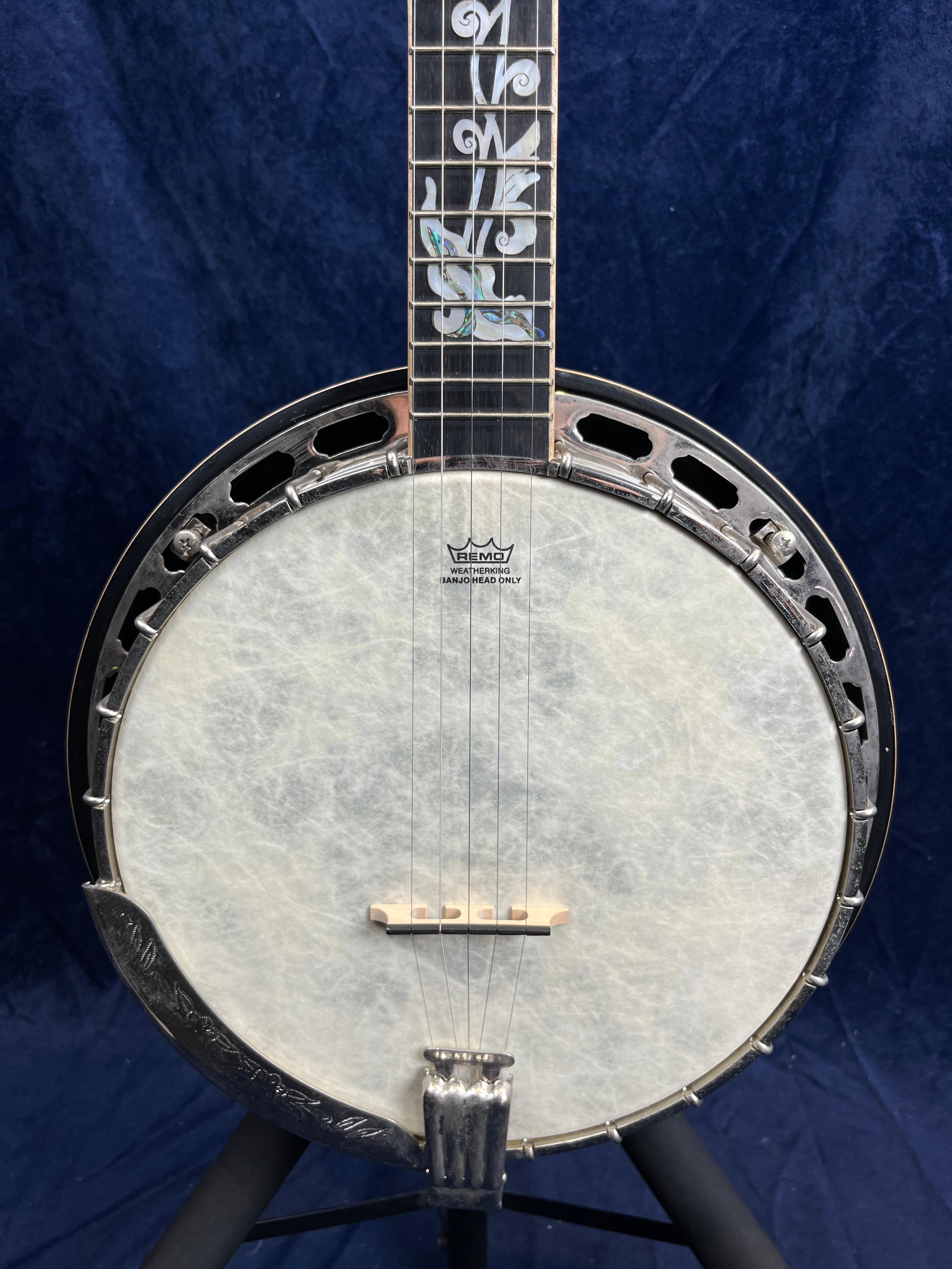 Banjo à 5 cordes avec peau blanche et décorations nacrées sur le manche, accastillage métallique argenté, fond bleu foncé.