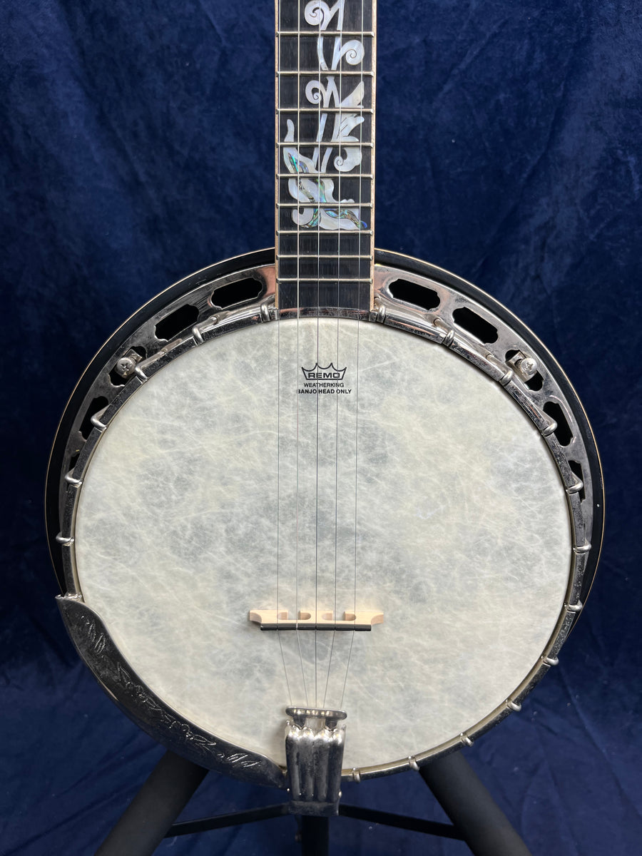 Banjo à 5 cordes avec peau blanche et décorations nacrées sur le manche, accastillage métallique argenté, fond bleu foncé.