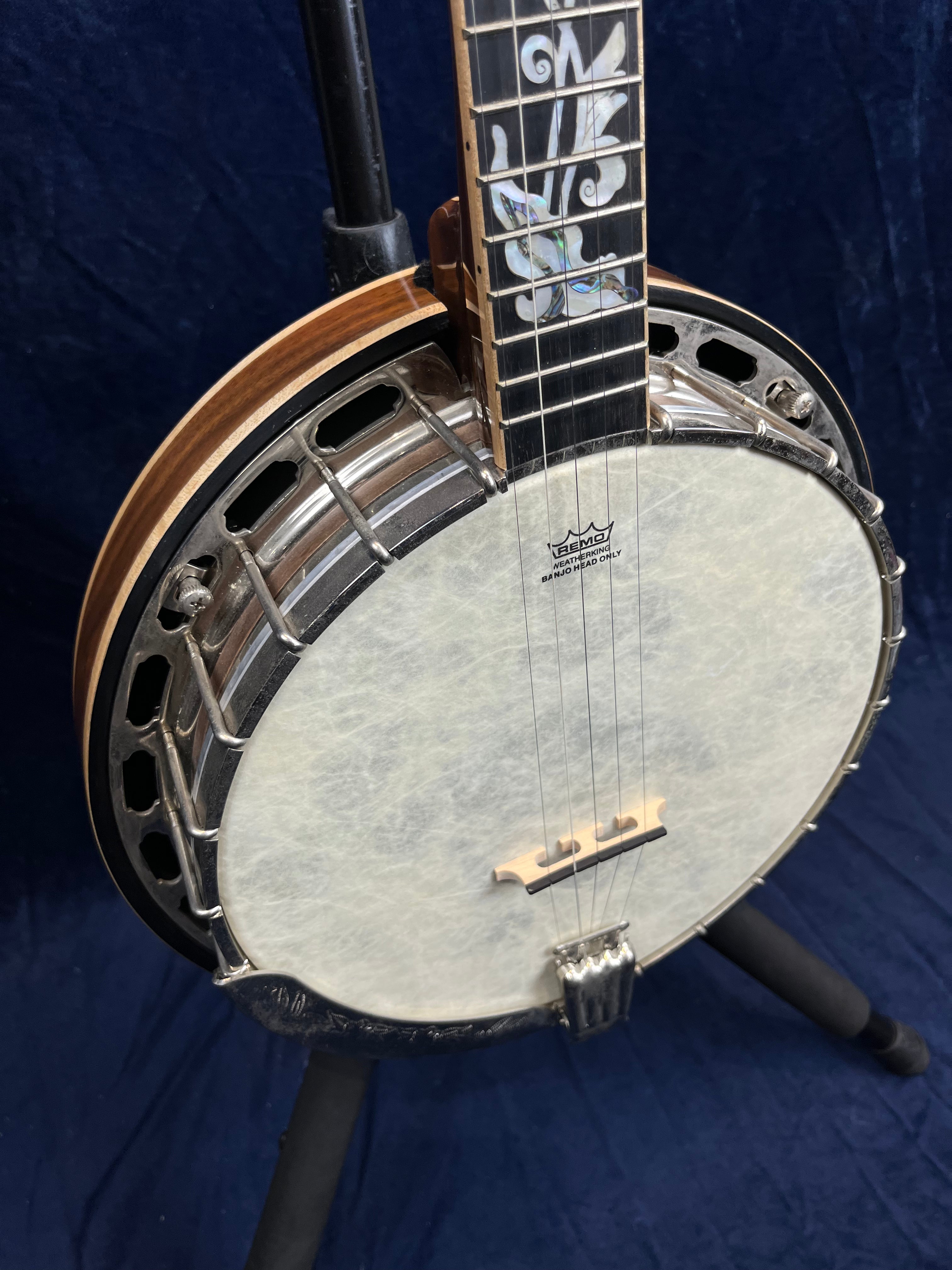 Banjo à cinq cordes avec caisse ronde, décor incrusté sur la touche et peau blanche tendue, posé sur un support noir.