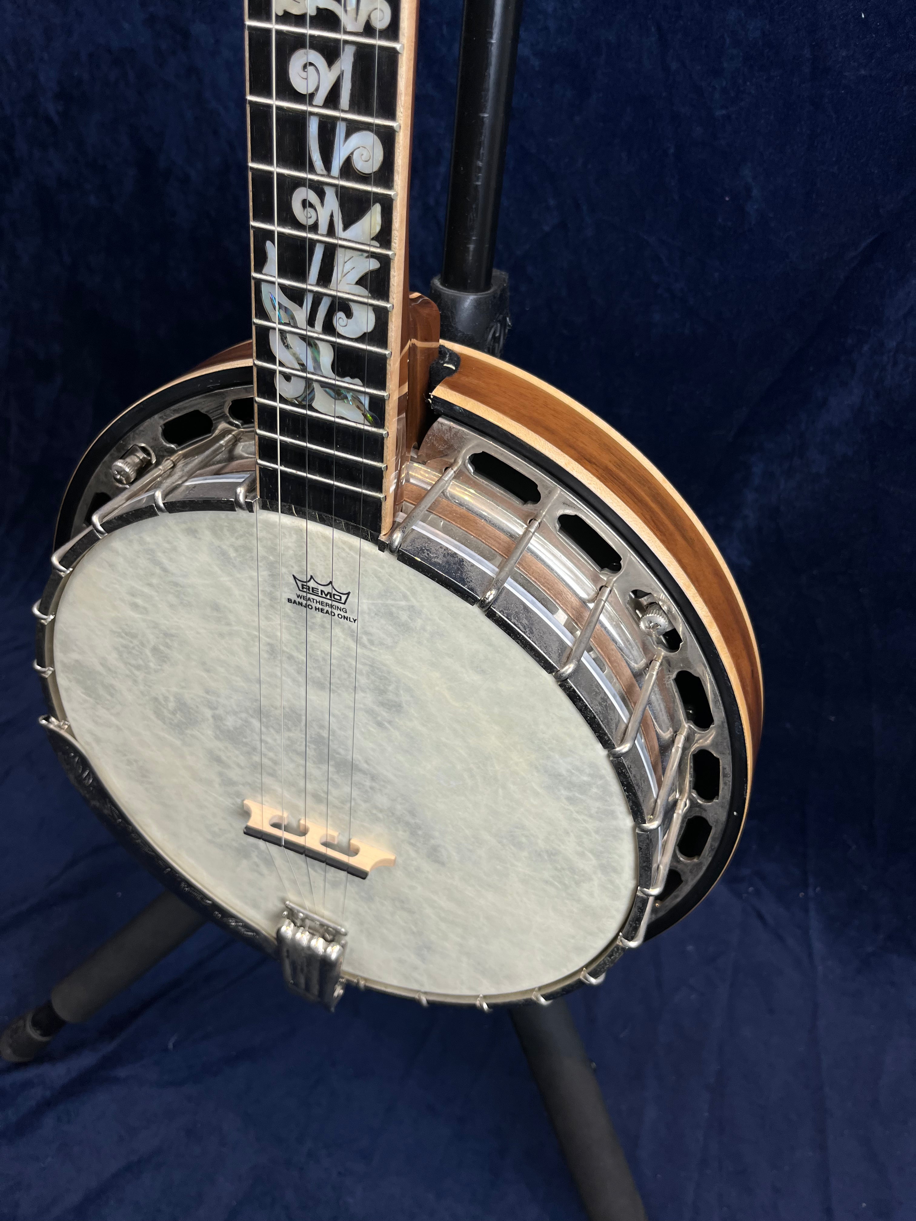 Banjo à cinq cordes avec manche orné d’incrustations blanches décoratives et caisse circulaire claire entourée d’un cerclage métallique.