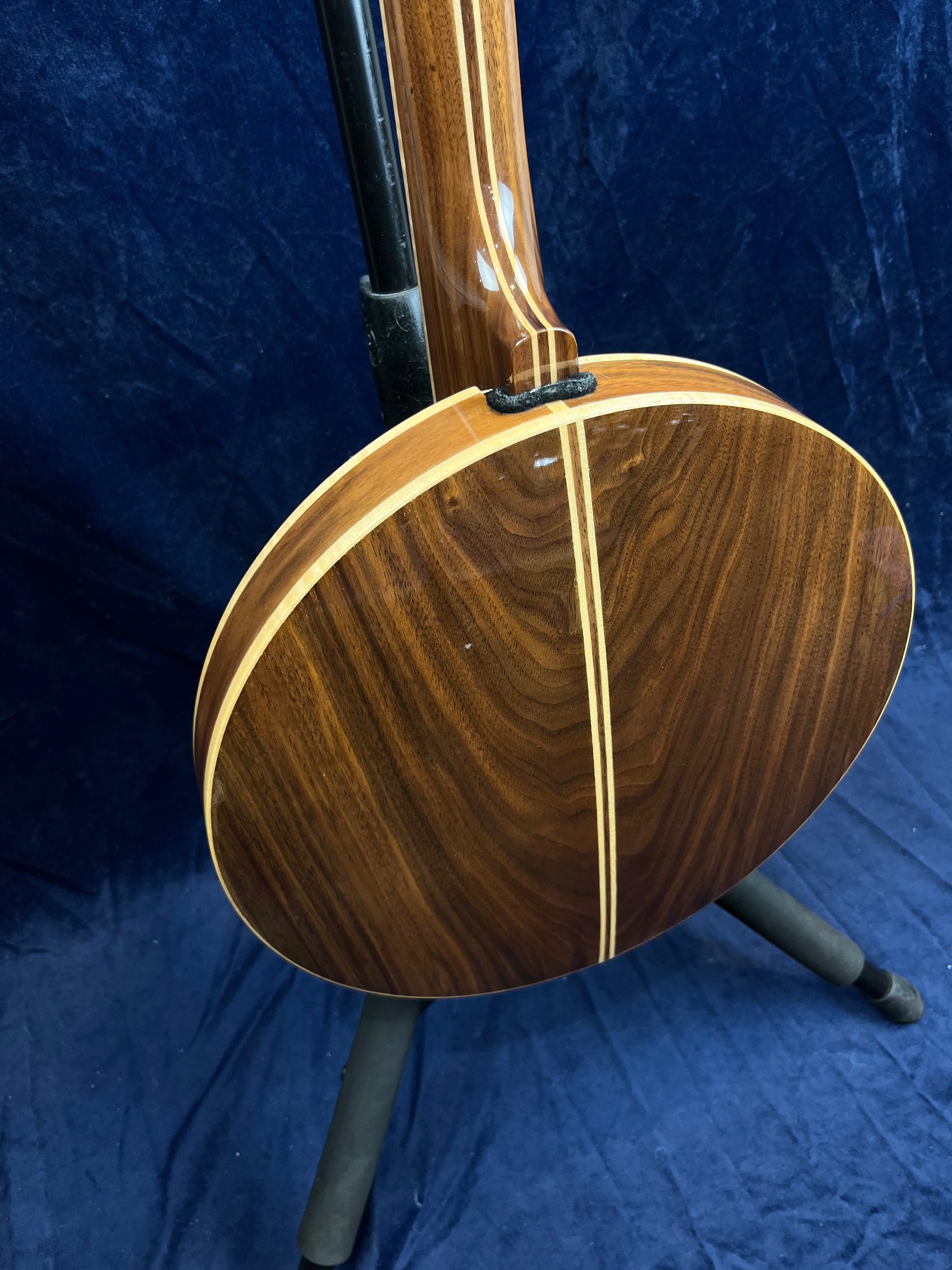 Banjo en bois verni avec motif à rayures claires sur le dos, posé sur un support noir devant un fond bleu.