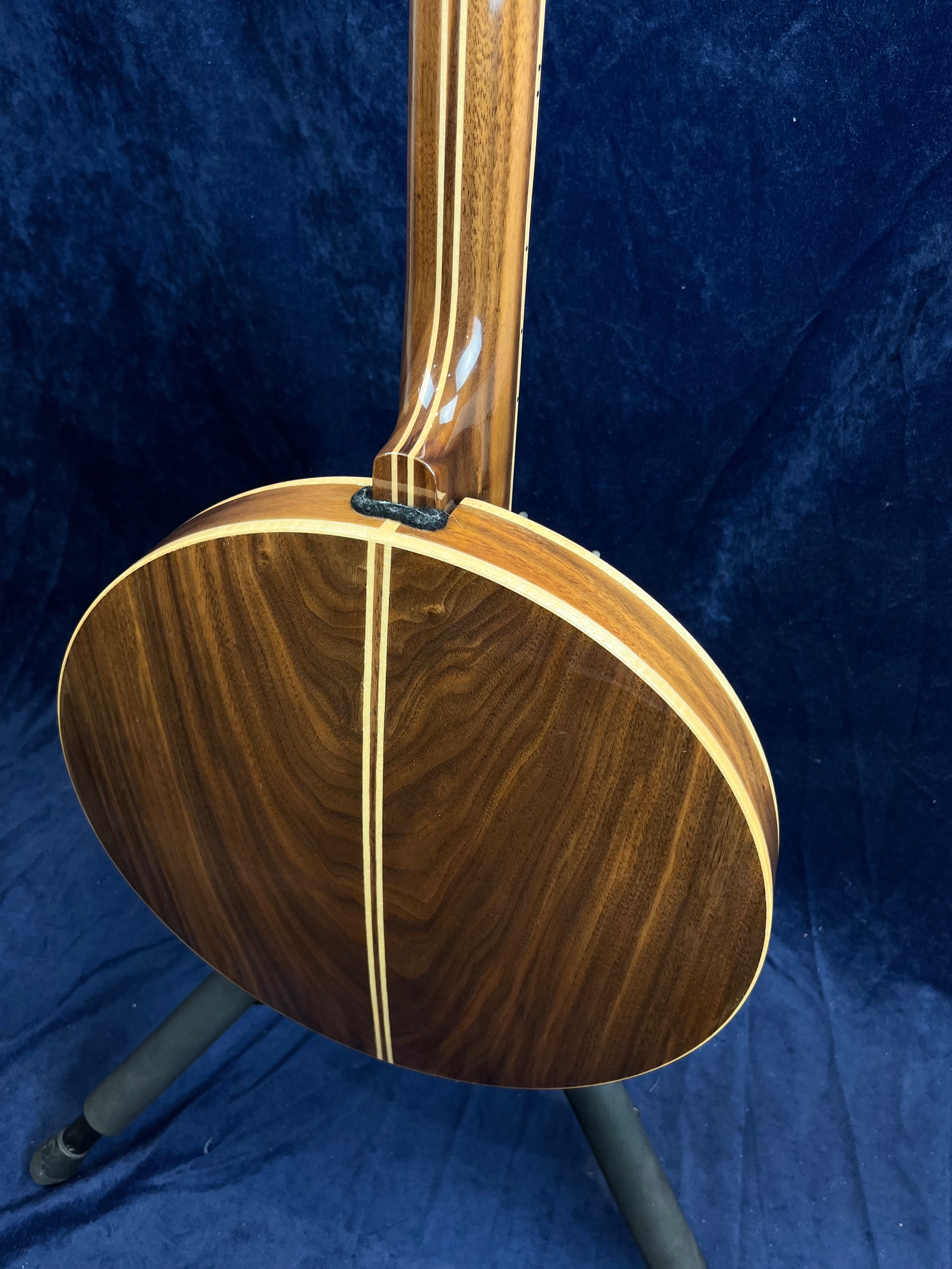 Banjo vu de dos, bois foncé brillant avec deux bandes claires verticales au centre, posé sur un support, fond bleu foncé.
