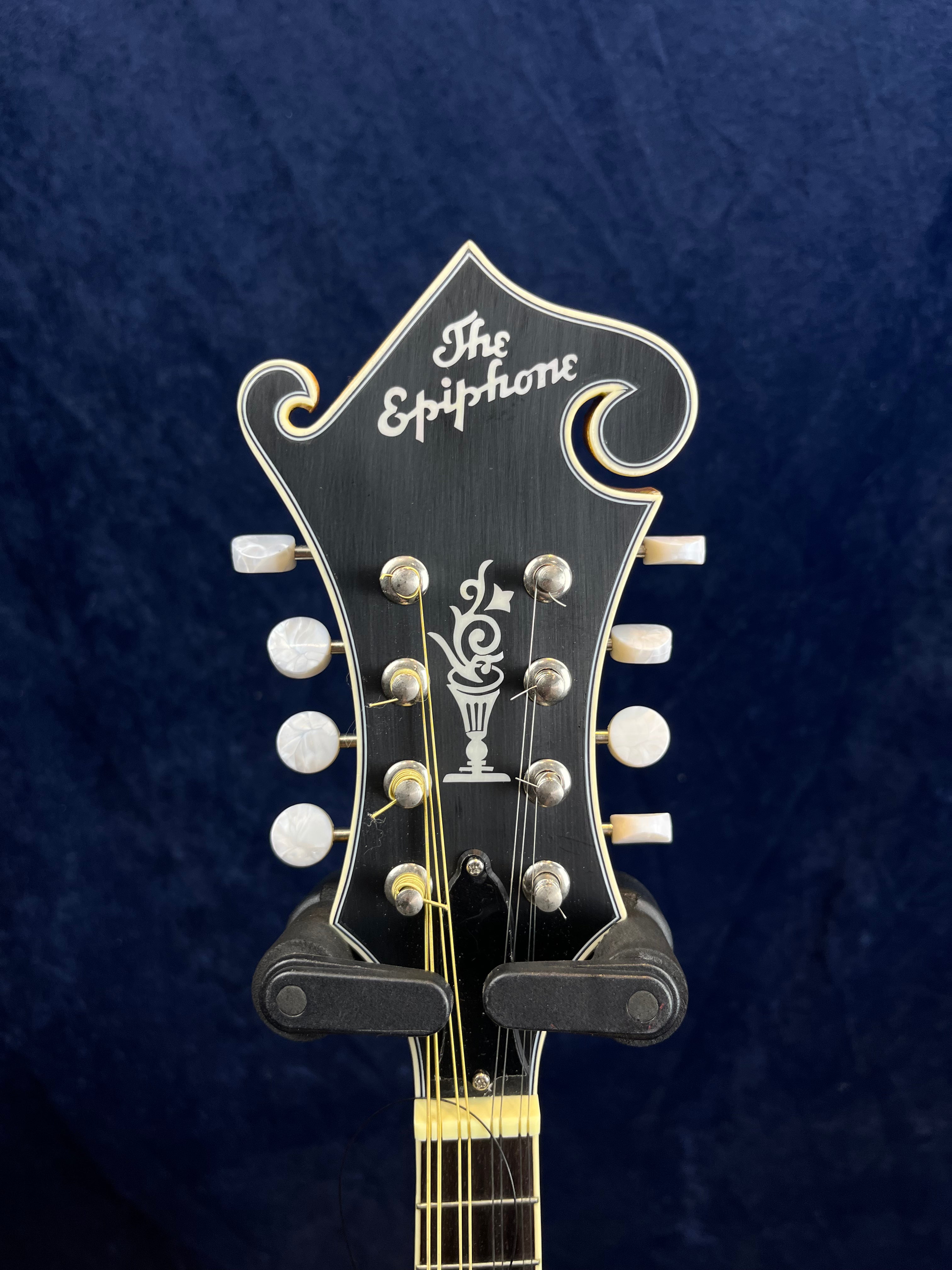 Tête de mandoline Epiphone noire avec incrustations blanches, huit mécaniques rondes nacrées et logo “The Epiphone” stylisé en haut.
