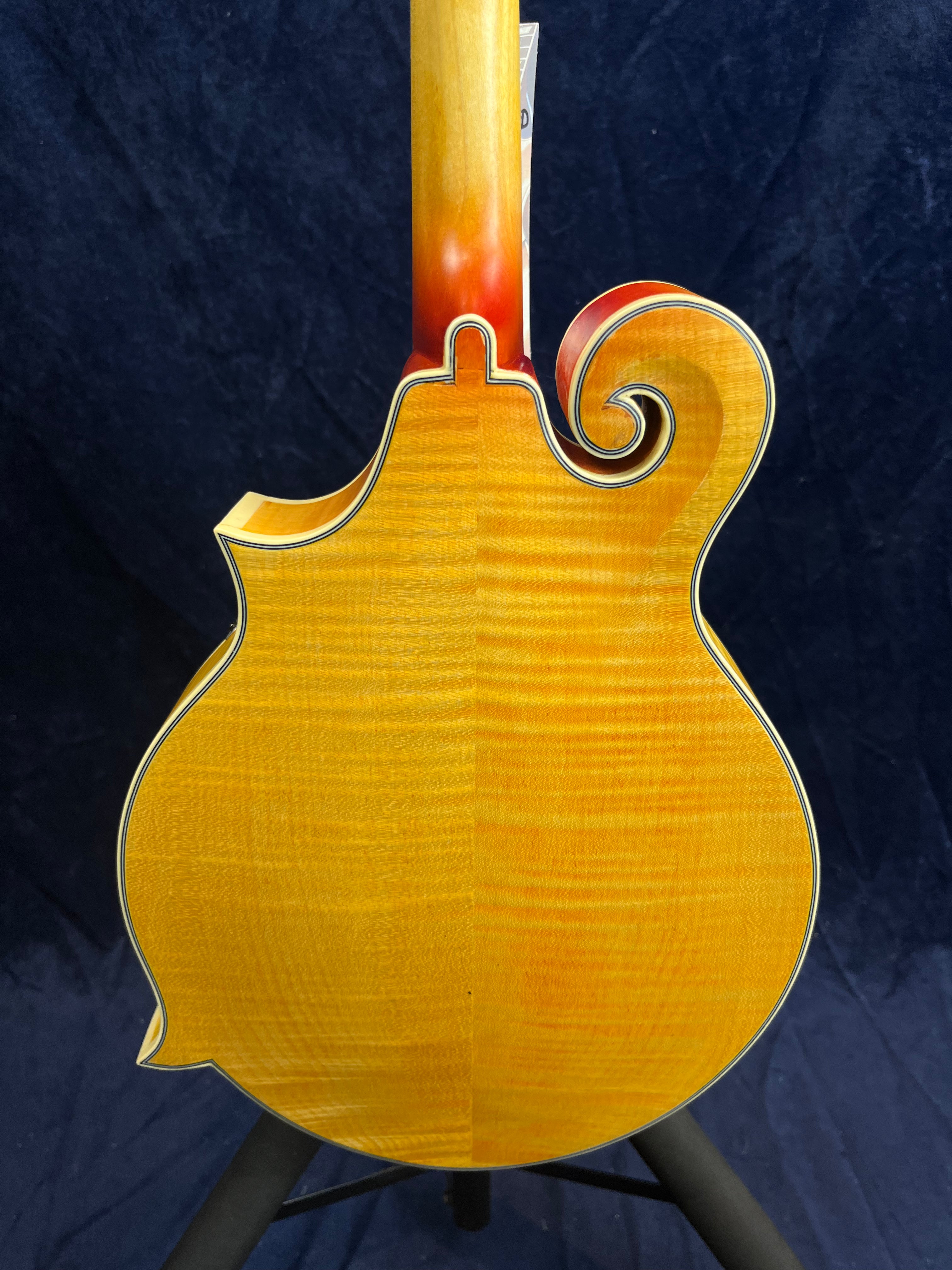 Mandoline à dos bombé en bois clair verni, décorée de liserés noirs et blancs, avec une volute sculptée sur le côté droit du corps.