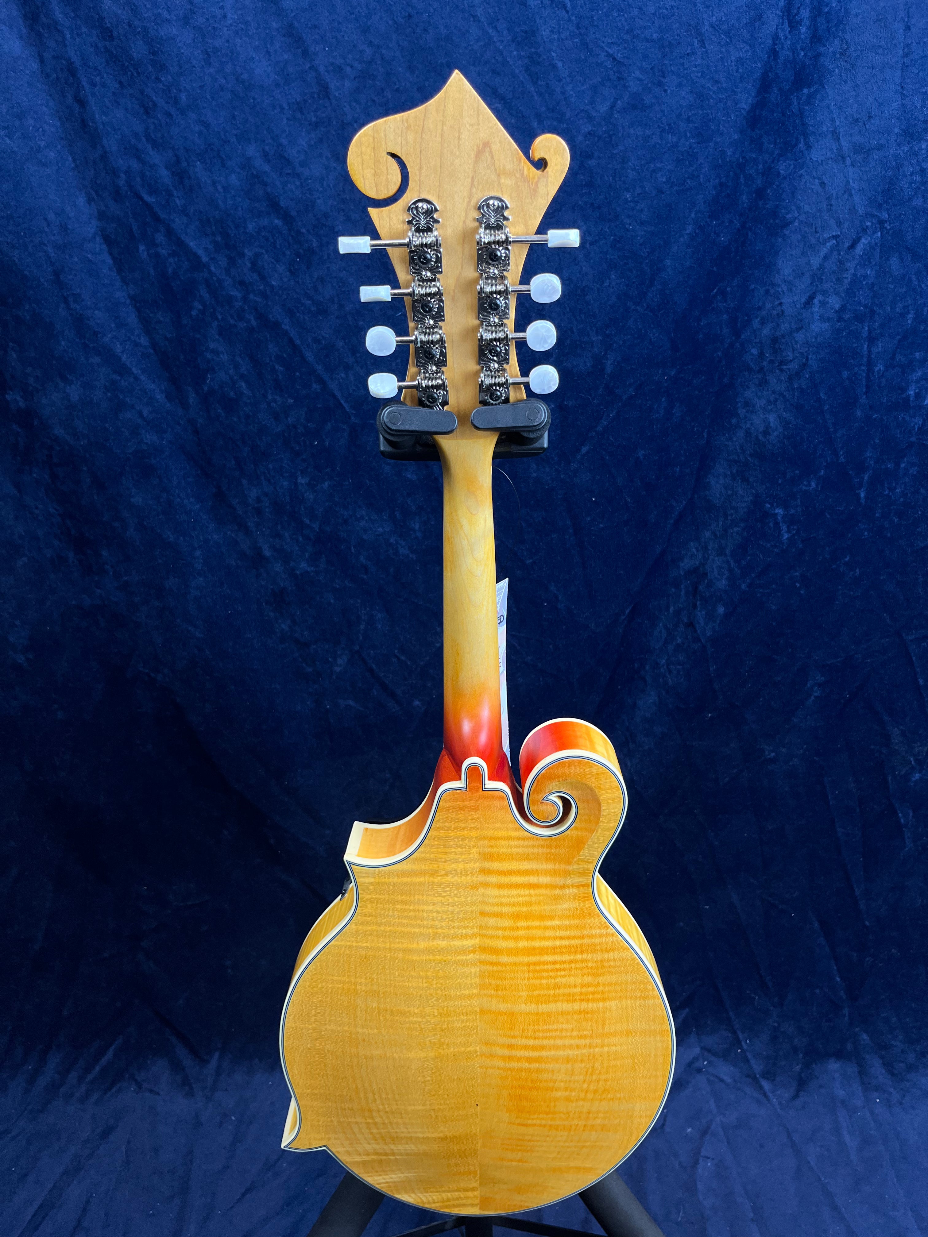 Mandoline vue de dos, bois clair verni avec motifs ondulés, contours blancs et une forme ornée de volutes sculptées.