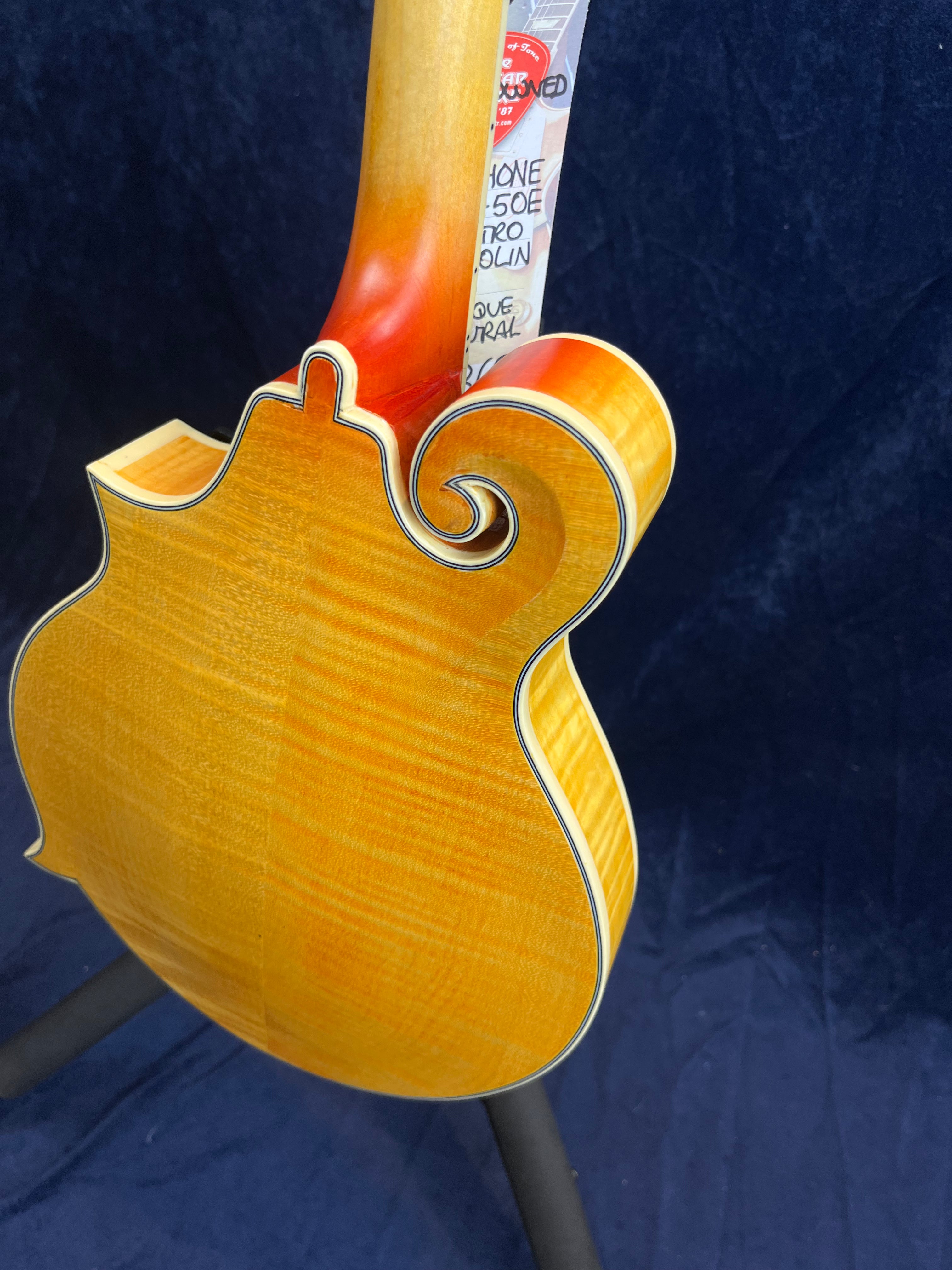 Mandoline à dos sculpté en bois clair, vernis brillant, avec une bordure noire et un motif en volute caractéristique sur le côté supérieur.