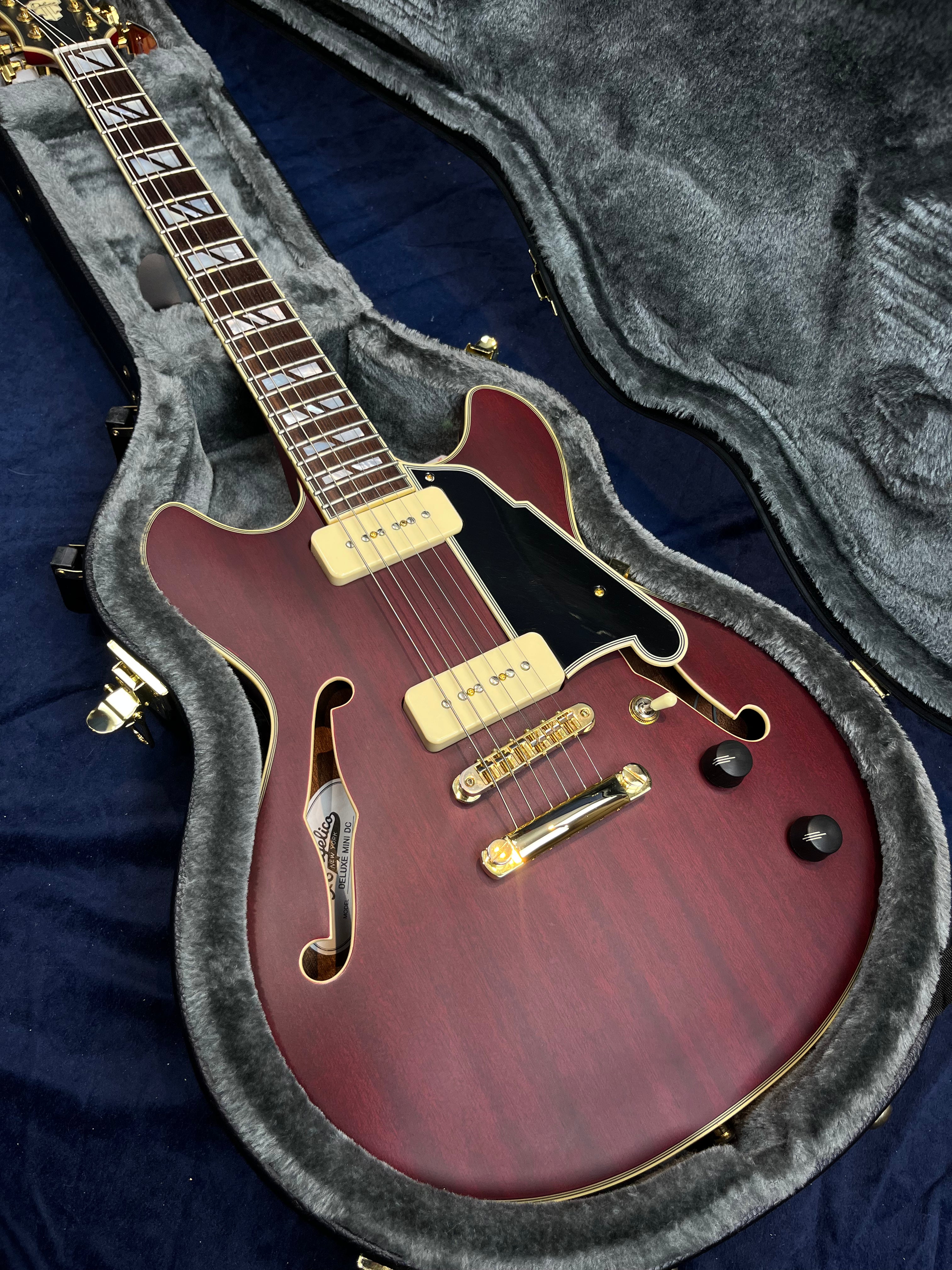 Semi-hollow electric guitar in a plush case, red finish, gold hardware, two cream pickups, black pickguard, two knobs, and split block inlays.