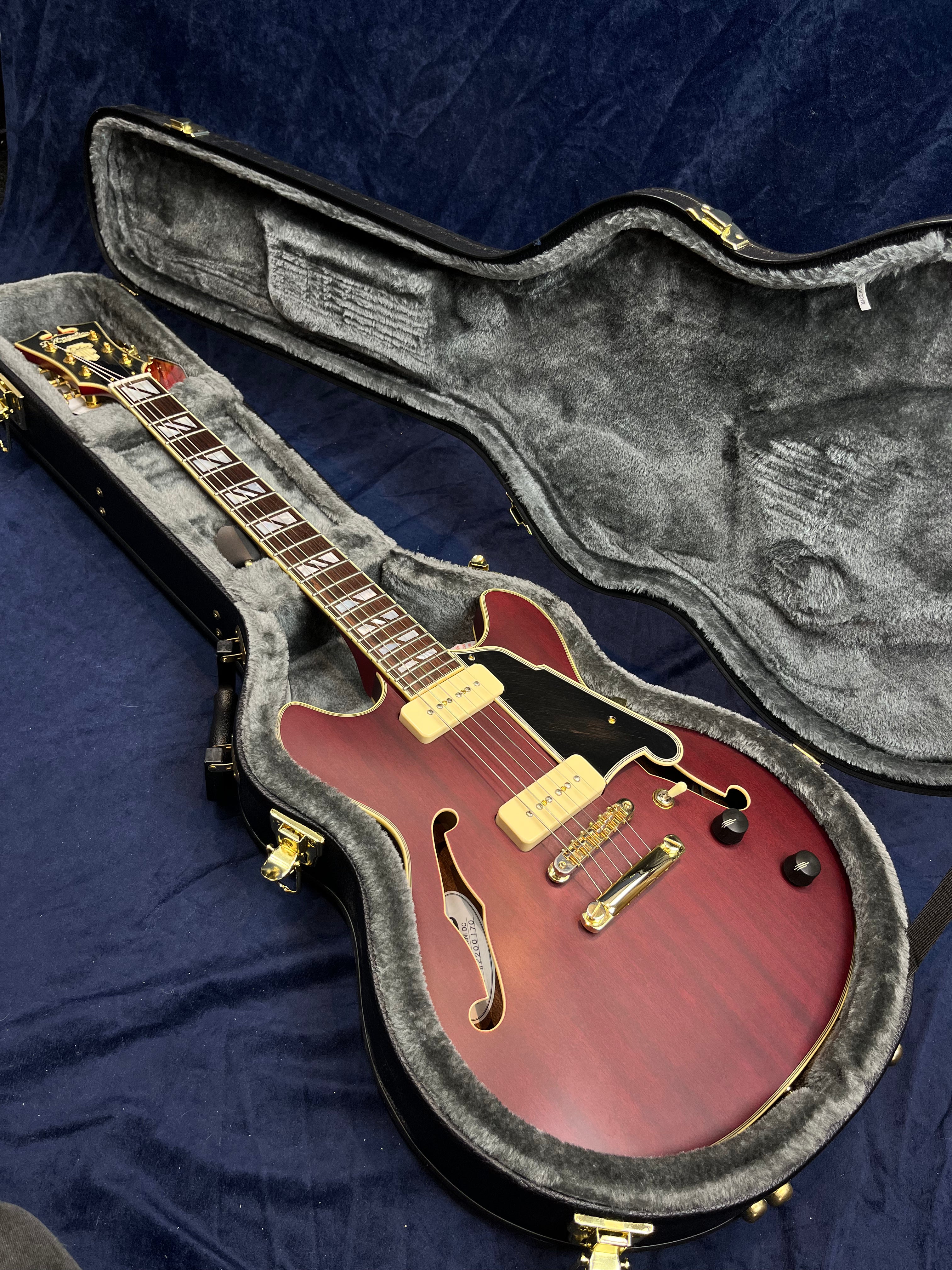 Semi-hollow body electric guitar with a red sunburst finish, gold hardware, and two pickups, resting in a plush gray hard case.