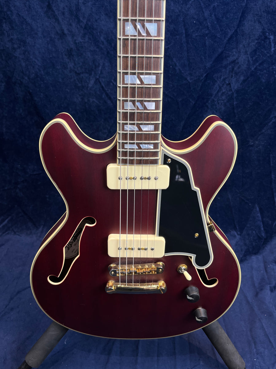 Semi-hollow electric guitar with deep red finish, cream pickups, gold hardware, black pickguard, dual f-holes, and block inlays on the fretboard.