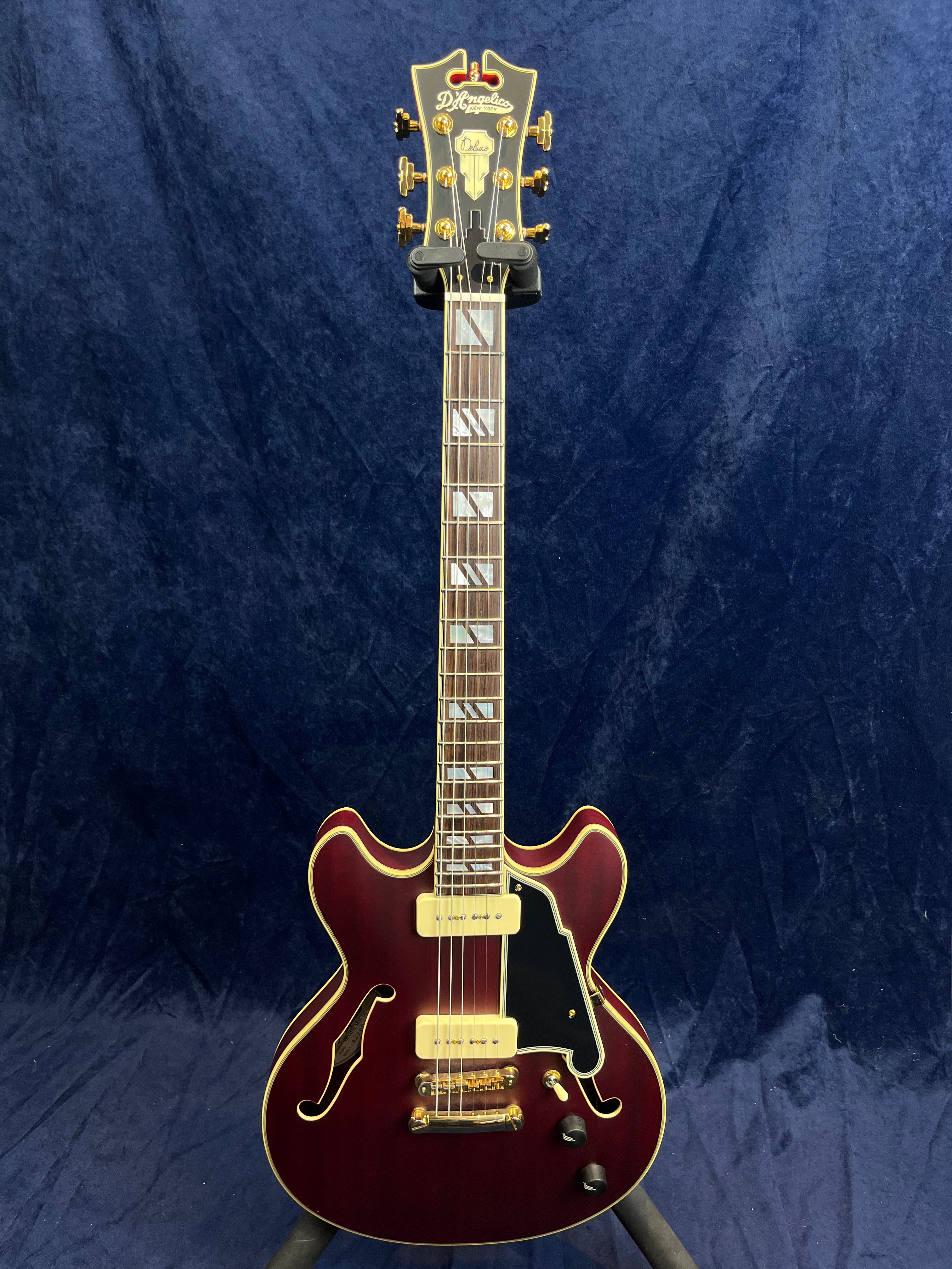 Semi-hollow electric guitar with a deep red body, gold hardware, two cream pickups, black pickguard, and block inlays on the neck.