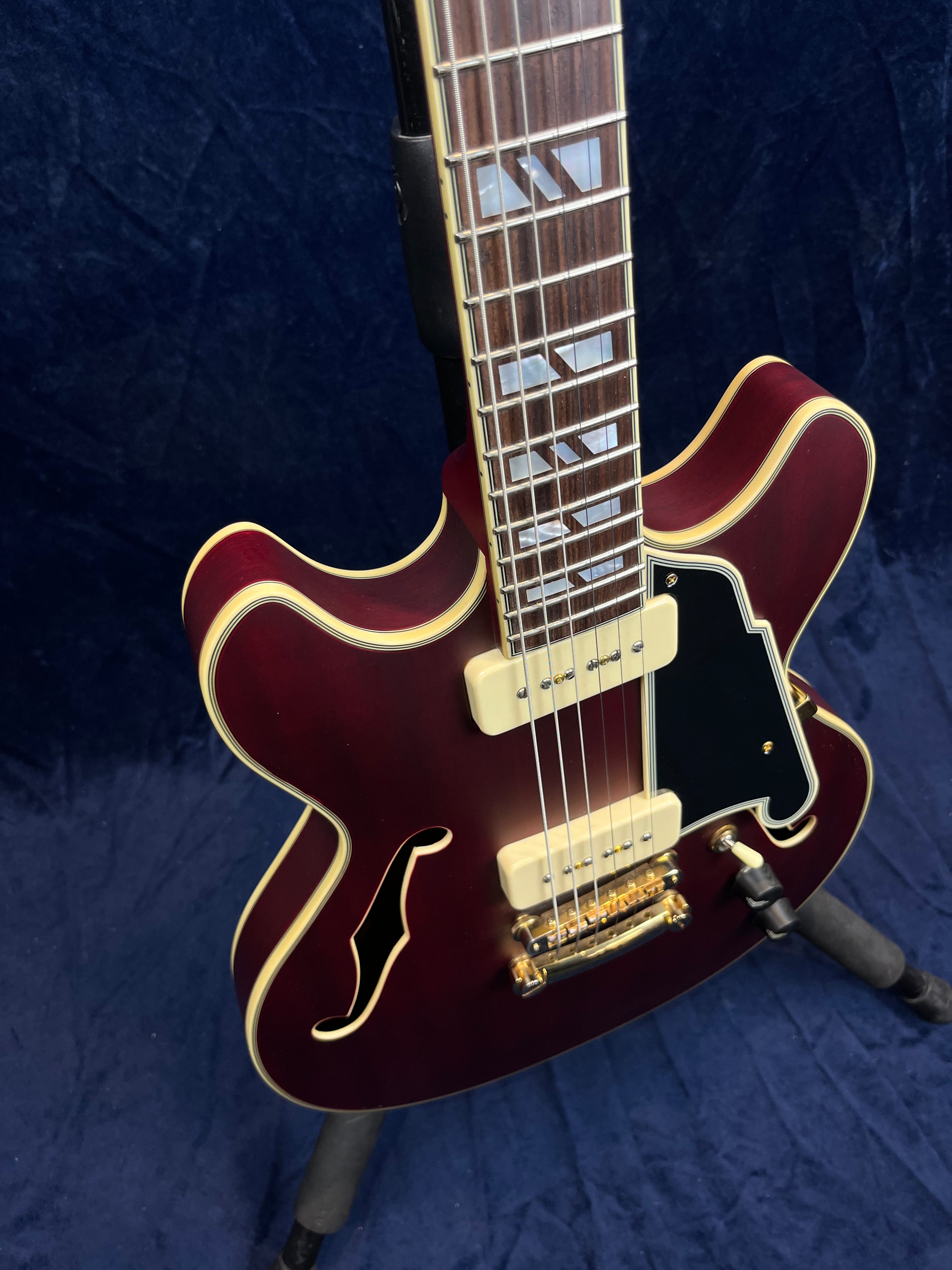 Semi-hollow body electric guitar in deep wine red with cream binding, gold hardware, two cream pickups, and a black pickguard.